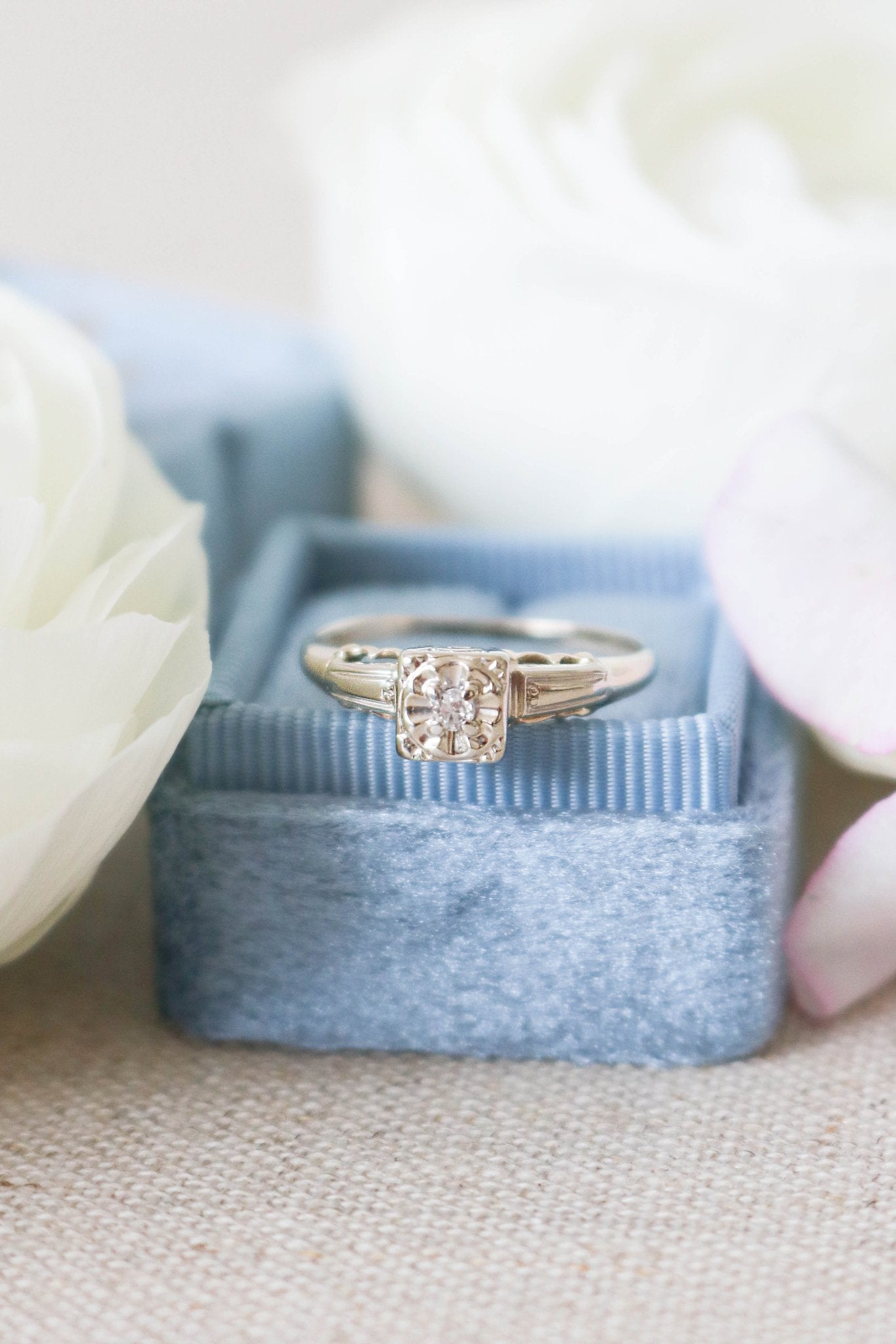 A Cayley Diamond Solitaire Vintage Engagement Ring in 14ct Gold, Art Deco Style from the 1930s sits atop a powder blue ring box. 