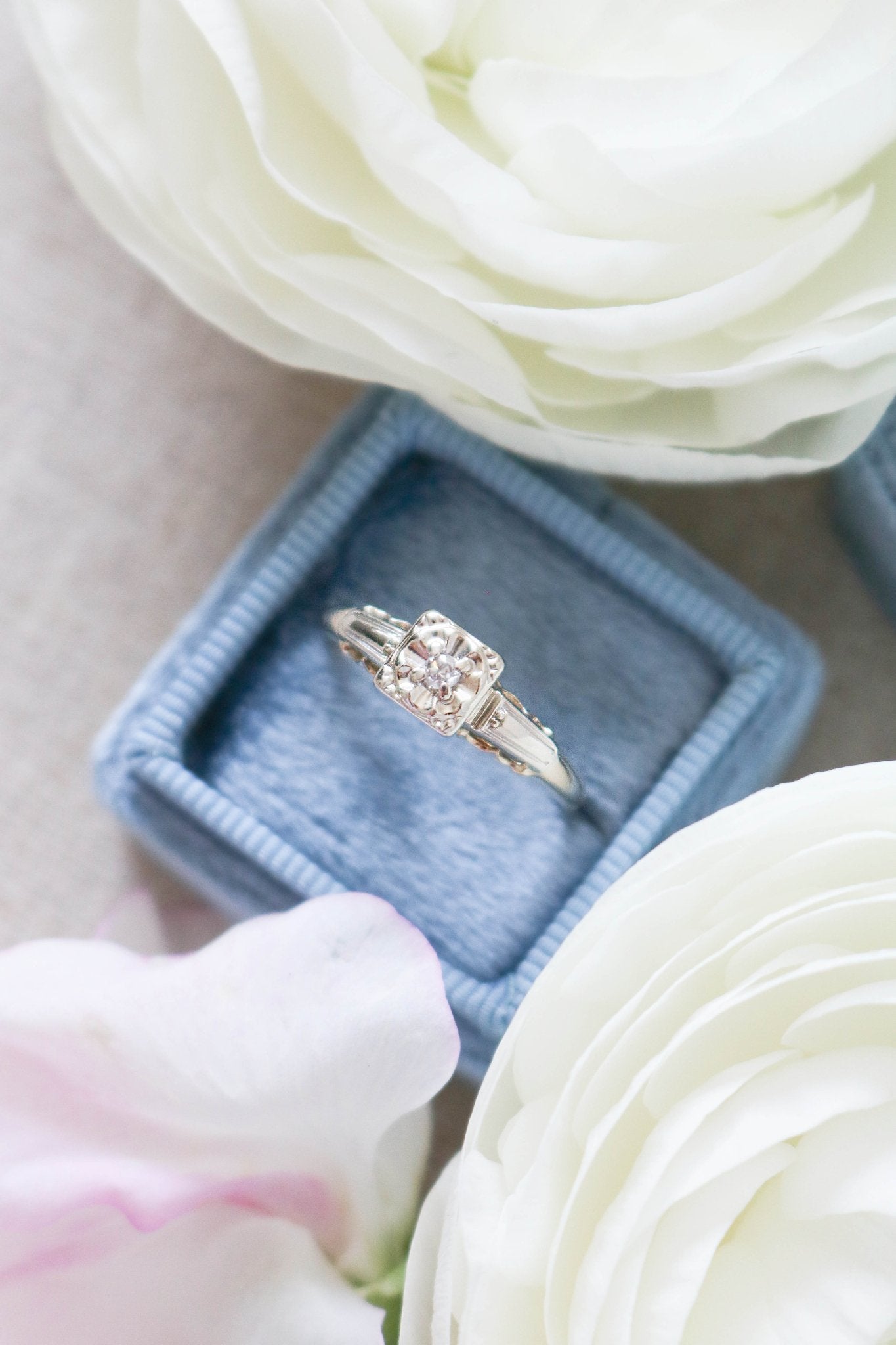 A Diamond Vintage Engagement Ring in Gold sits in a ring box surrounded by white roses. 