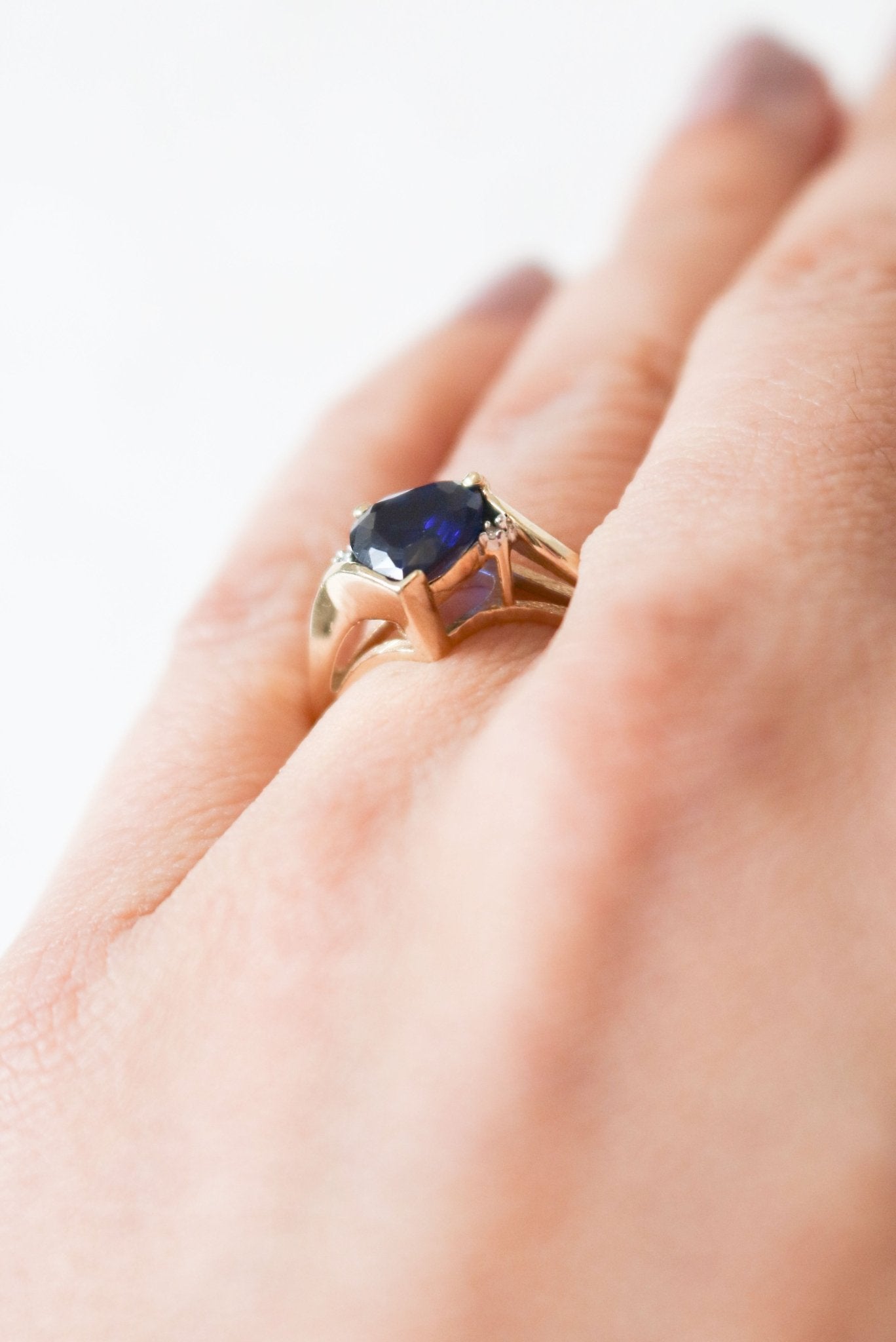 Close up of the Celia Sapphire Heart and Diamond Vintage Engagement Ring in 9ct Gold worn on a ring finger.