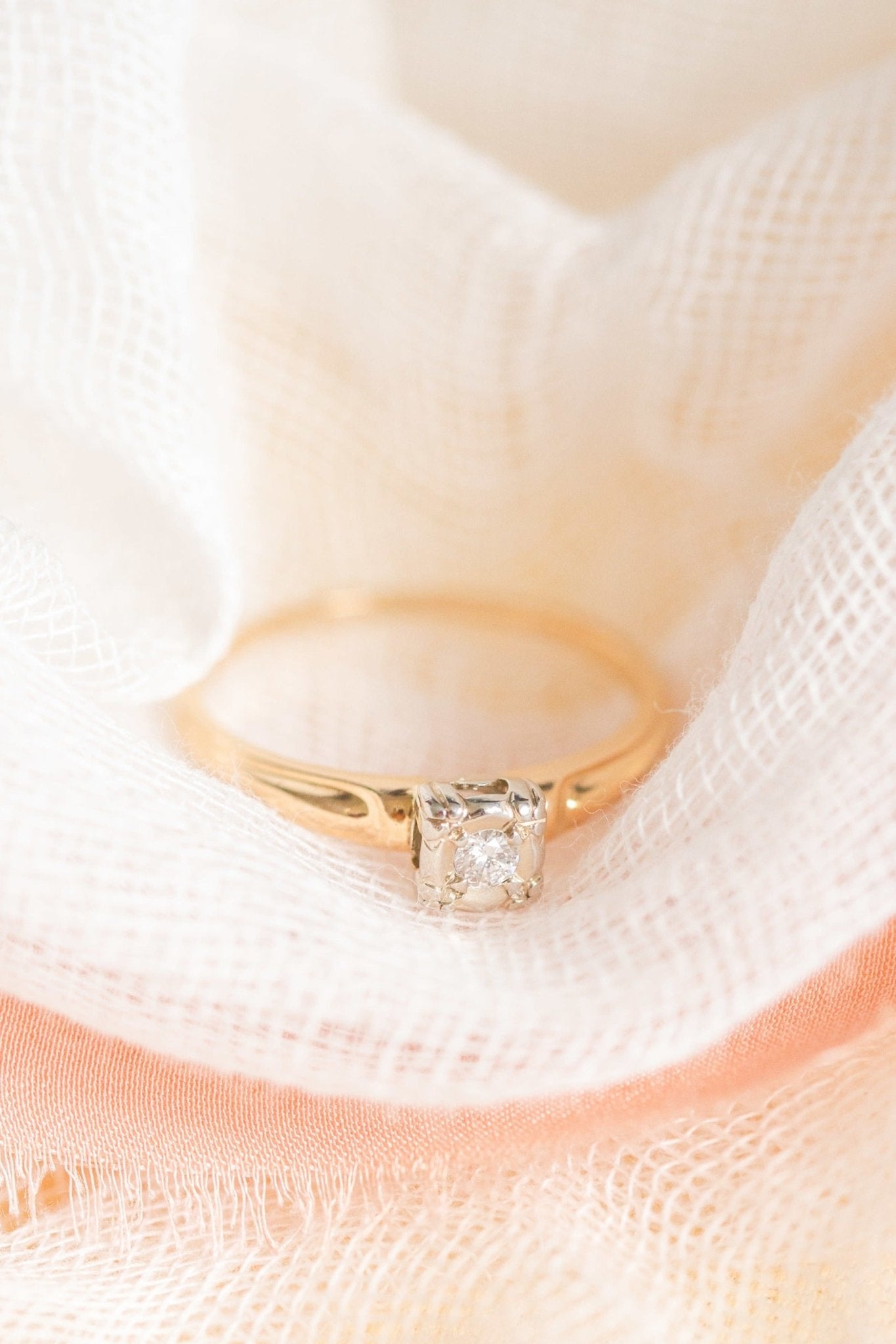 A Clara Solitaire Diamond Engagement Ring in 14k Gold c. 1930s Art Deco is nestled in a white fabric. 