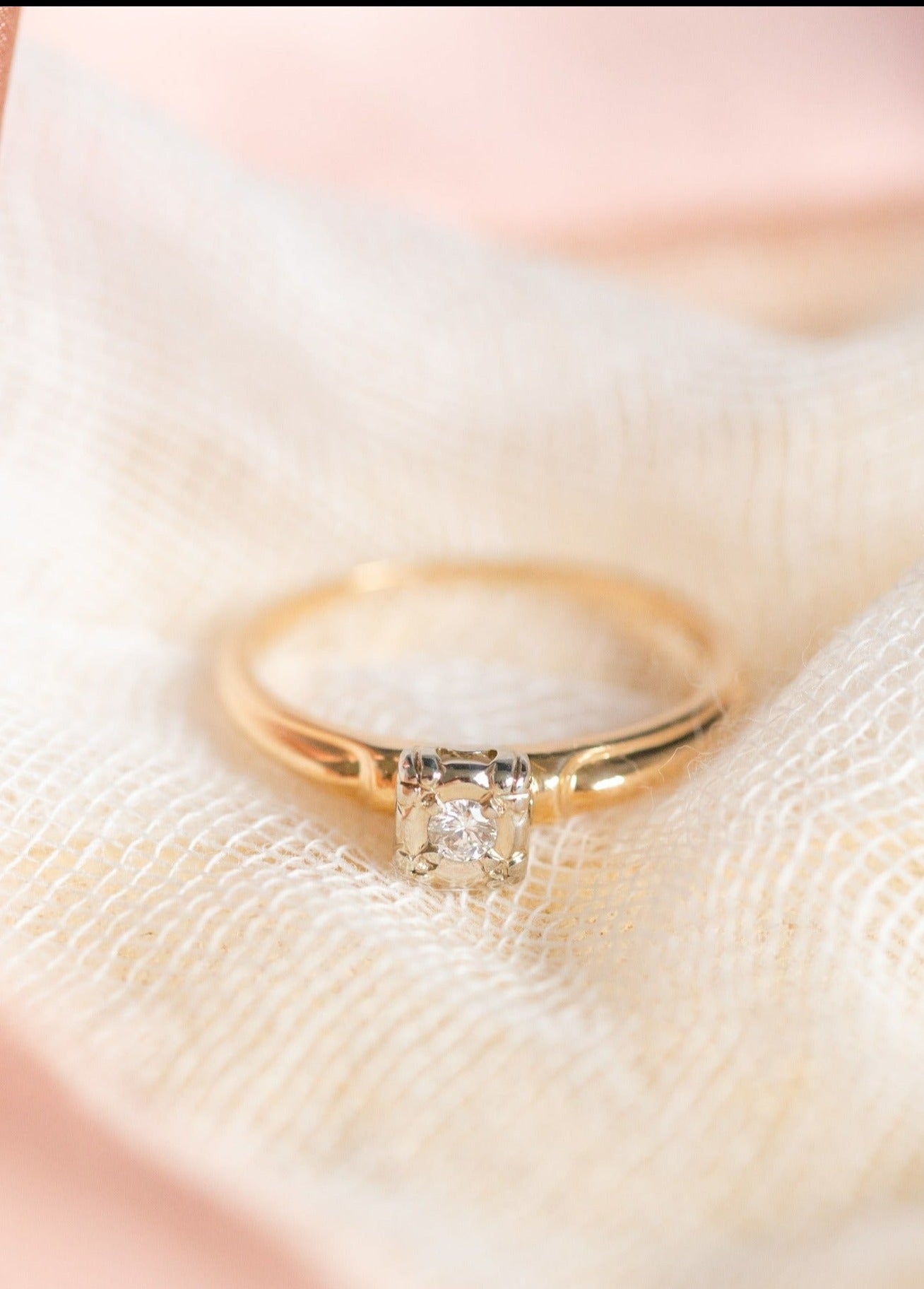 A Clara Solitaire Diamond Engagement Ring  c. 1930s Art Deco in 14k Gold is nestled in a white fabric. 