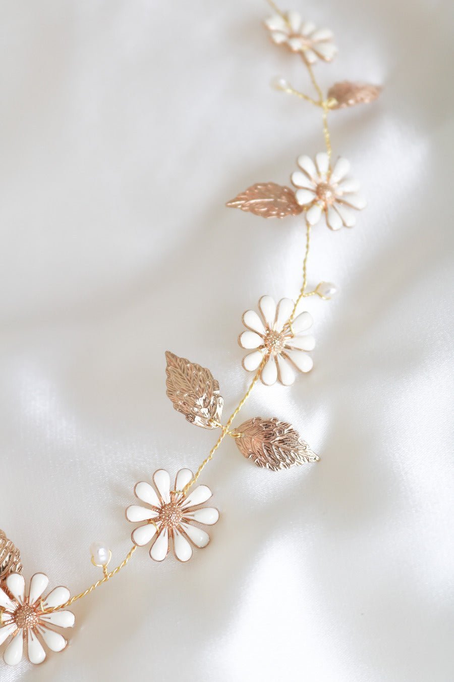 A close up of a Gold Daisy Chain Hairvine with Fresh Water Pearls against a white satin background. 