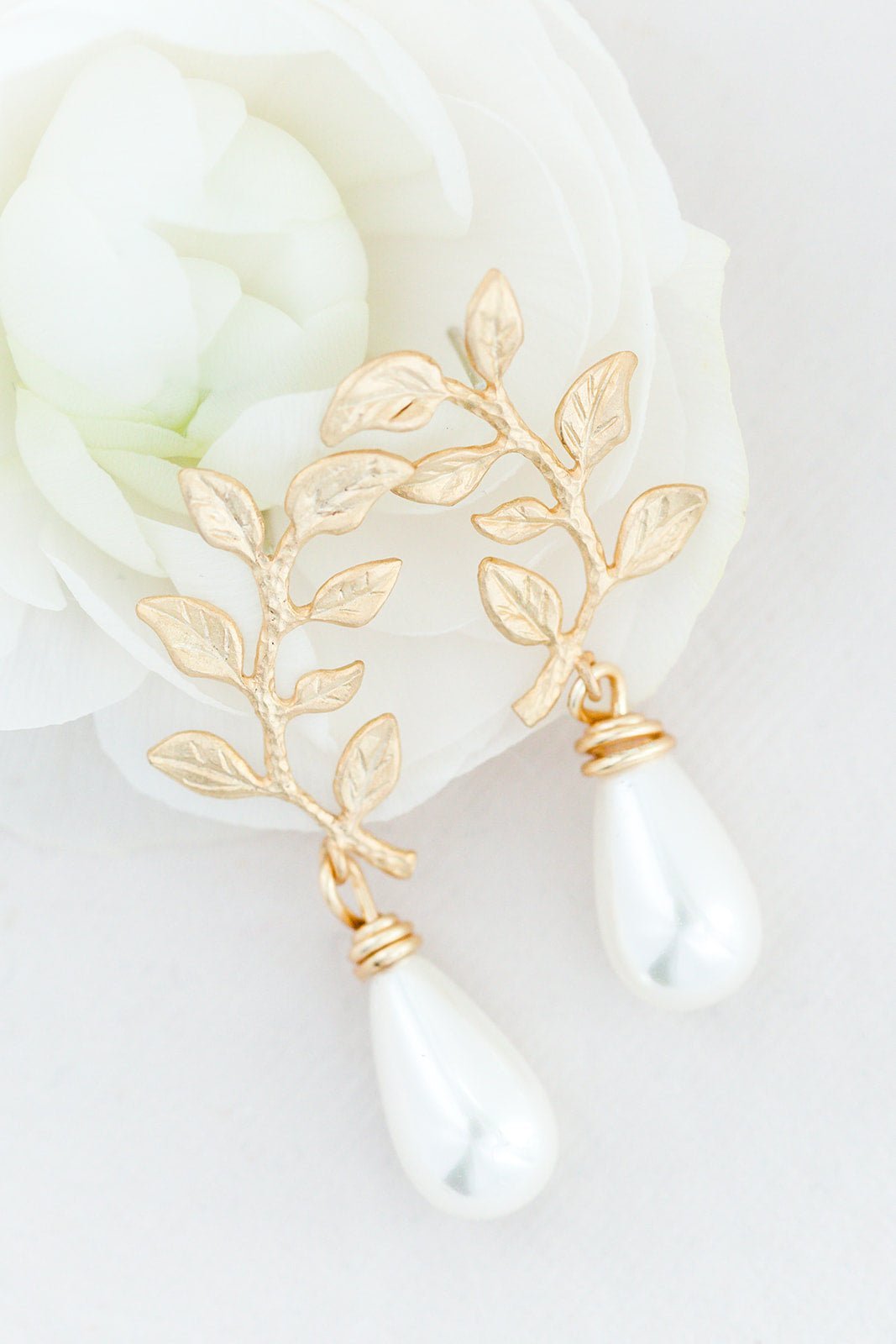 A pair of gold-filled leaf and freshwater drop pearl stud earrings displayed on a white rose & background. Pearl bridal earrings, organic pearl jewelry, & handmade Canadian jewelry by affordable Canadian jewelry brand
