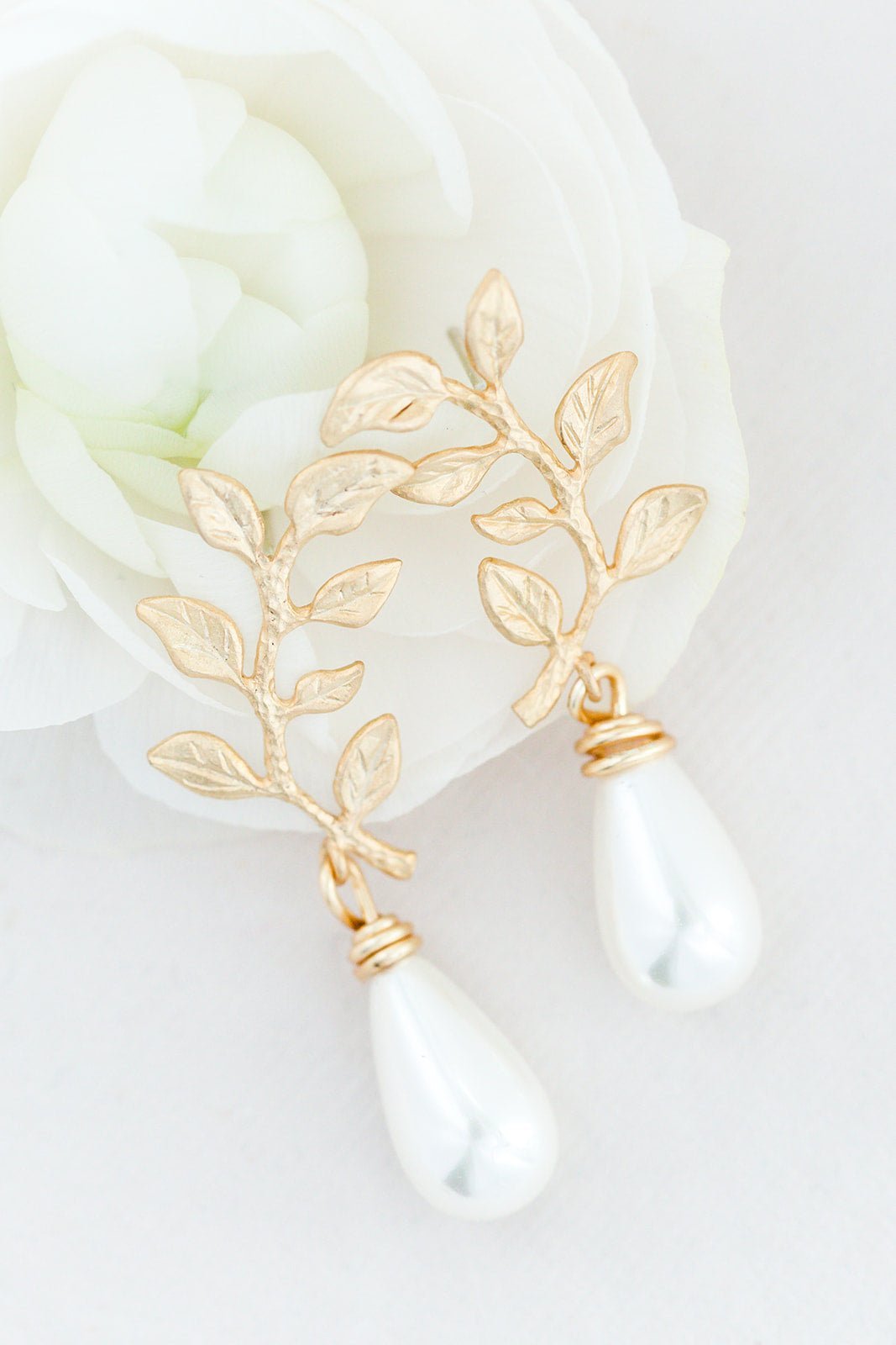 A pair of Daliyah Leaf & Drop Pearl Studs laying on a white rose. 