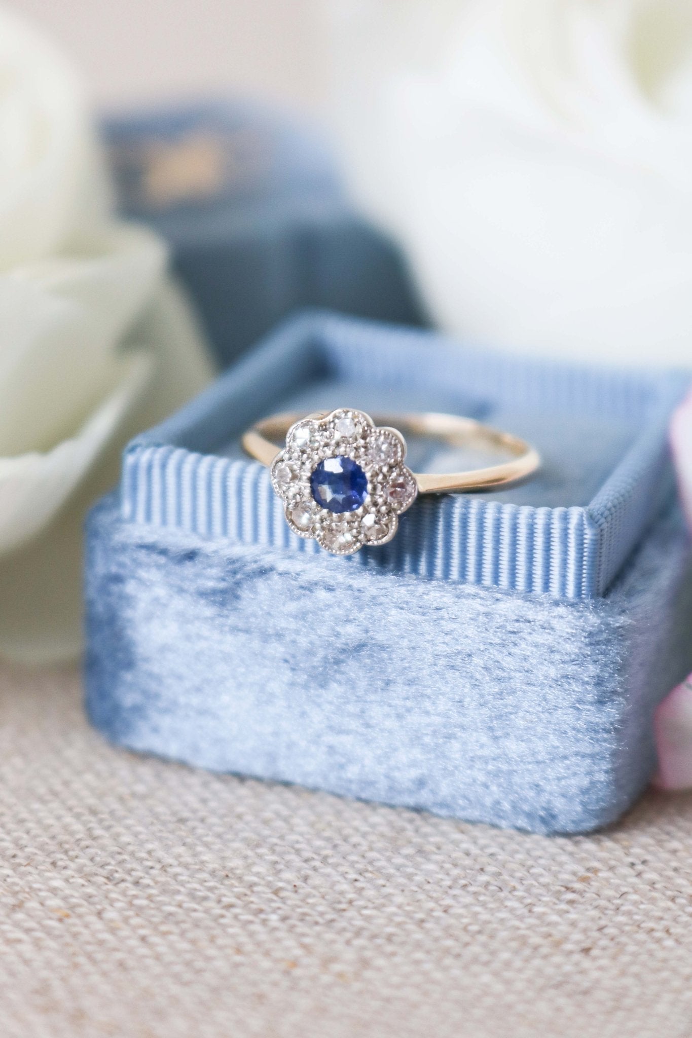 A close up front view of a 18k Yellow and White Gold Vintage Sapphire and Diamond Engagement Ring on top of a powder blue ring box. 