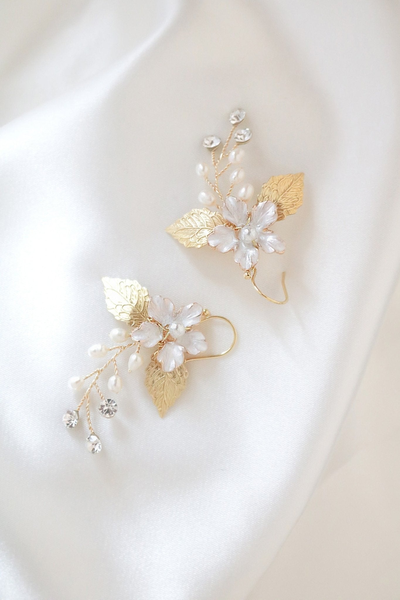 A pair of golden floral earrings with freshwater pearls and crystals against a white satin sheet. 