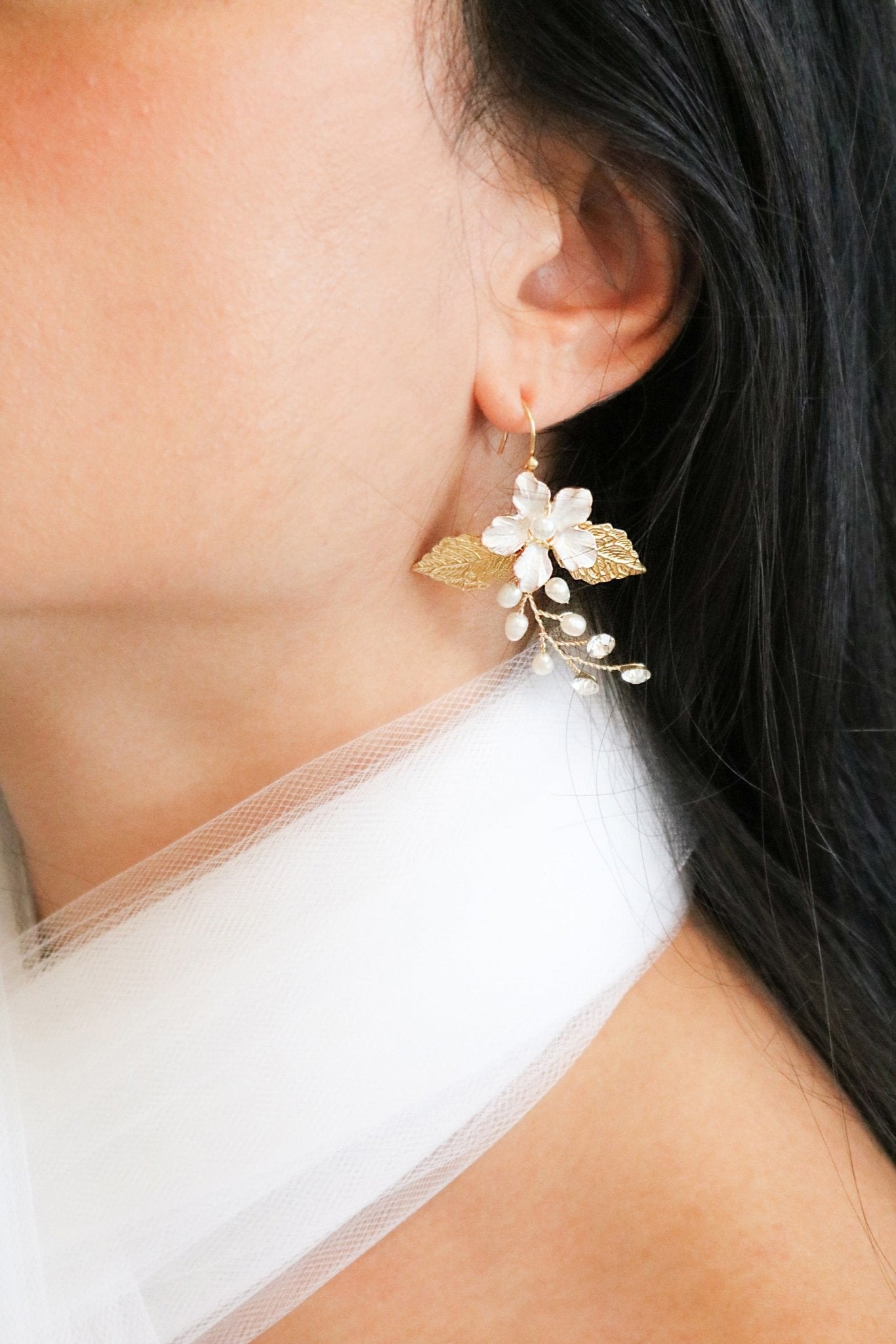 A statement bridal earring hangs from an earlobe with an enamel flower set in gold with freshwater pearls and crystals. 