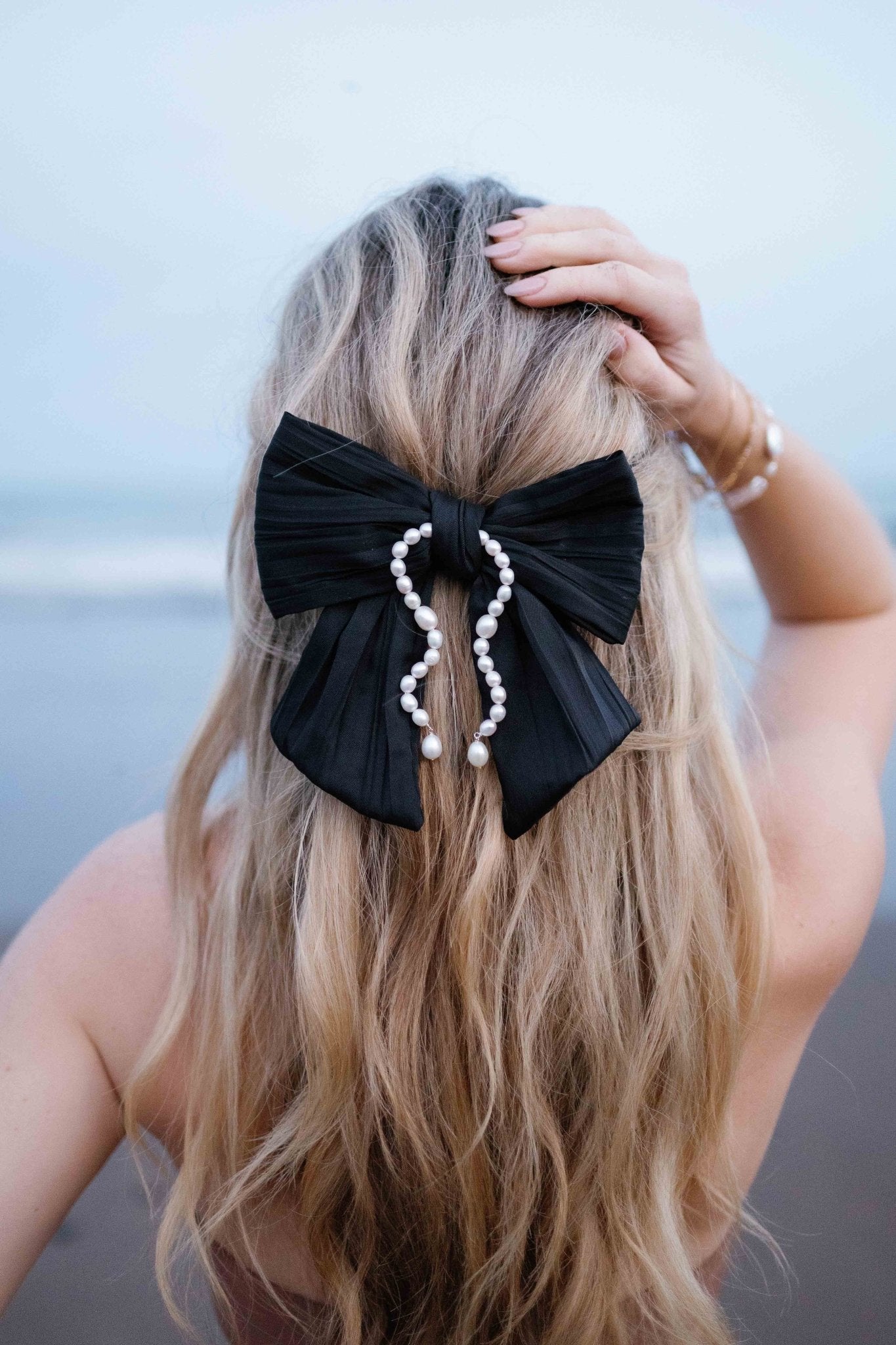 Woman wearing a black satin Delphine Bow with strung freshwater pearls.