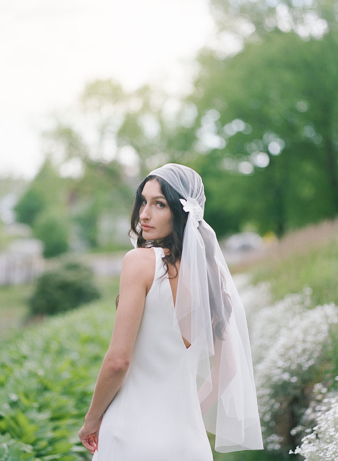 Bride looking back over her shoulder wearing a veil with bunched sides near the top with embroidered white flowers. 