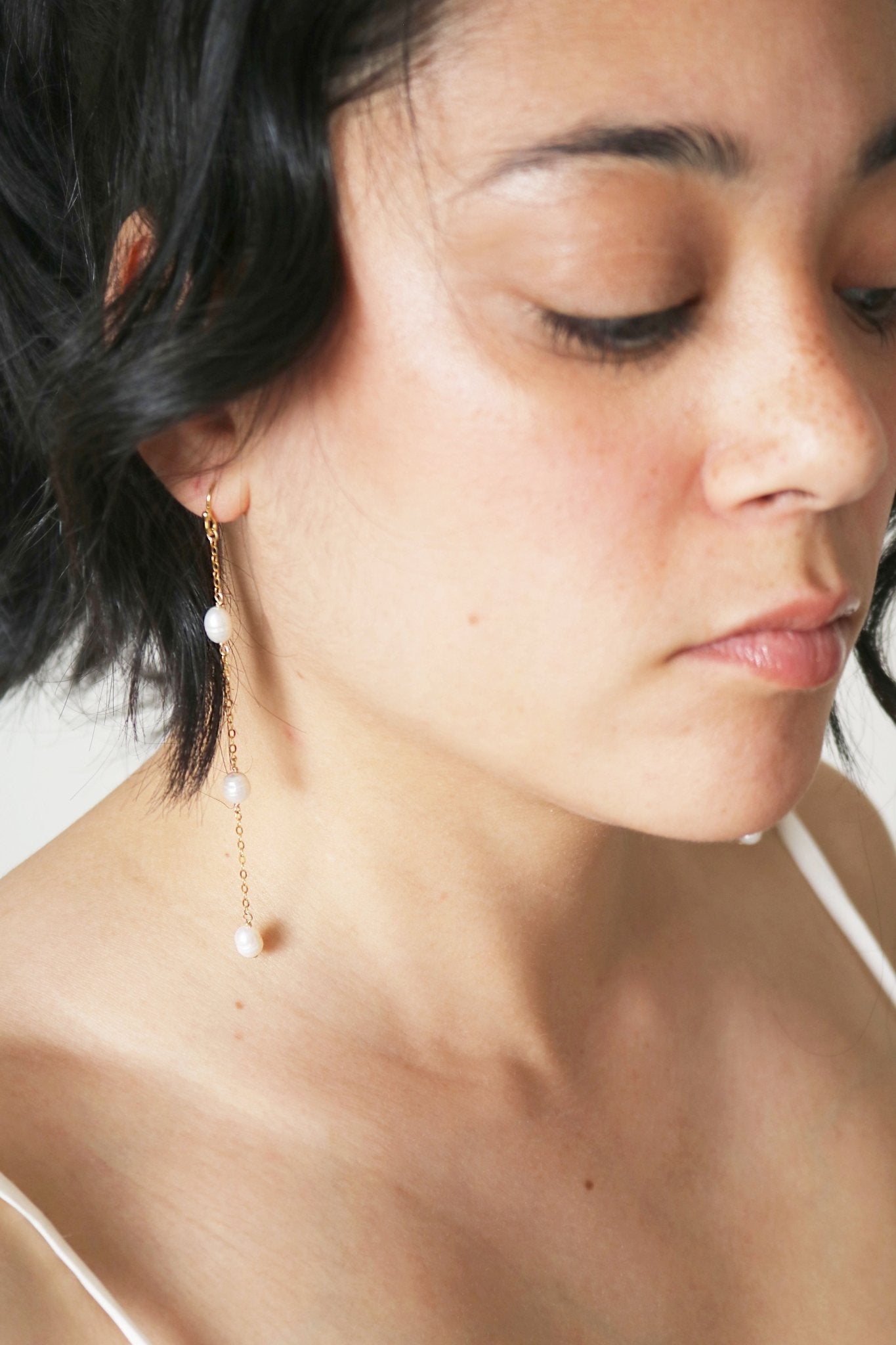 Gold-filled long drop earrings with staggered freshwater pearls hang from a woman's ear. 