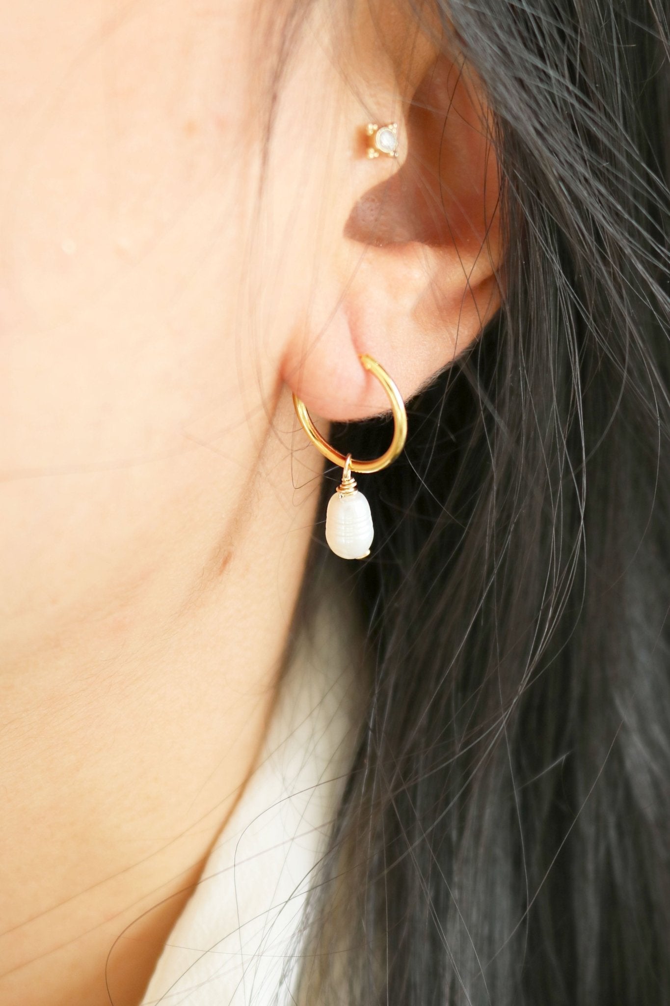 Gold-filled hoop earring with a single organic freshwater pearl sits in a woman's ear. 