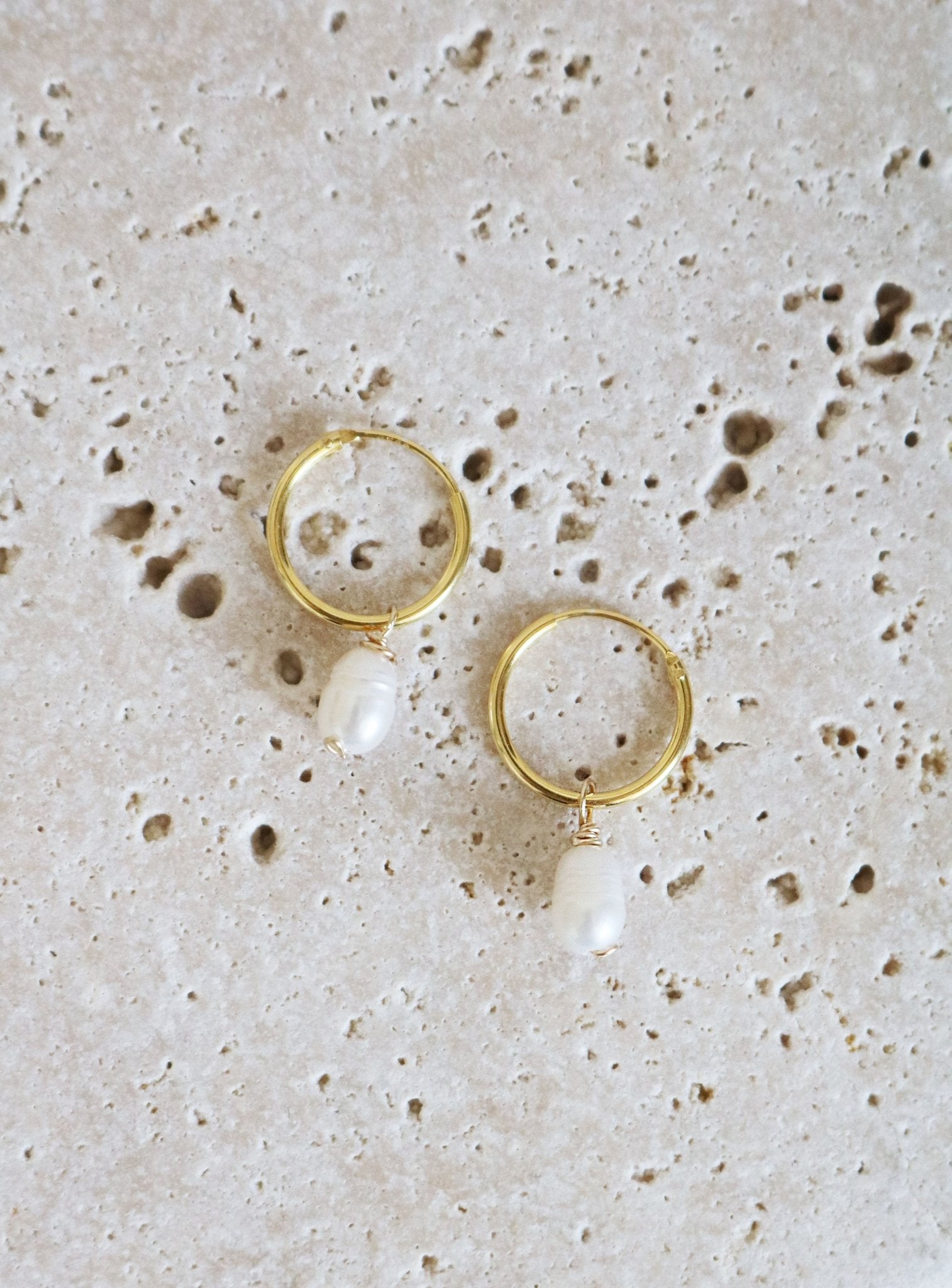 A Gold Filled Set of Dew Drop Fresh Water Pearl Hoops lay on Stone.