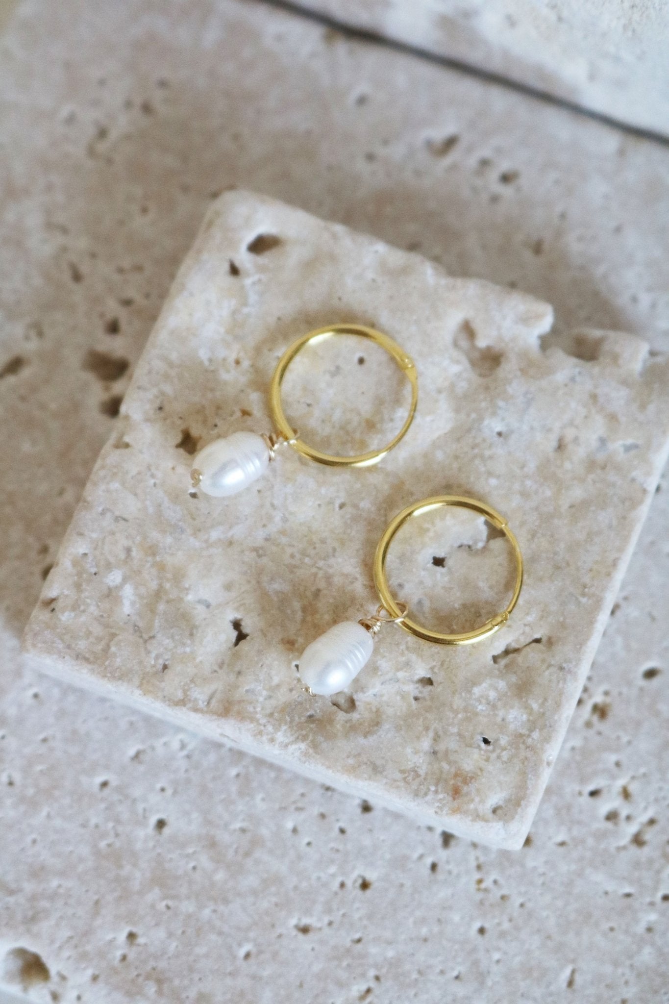 A Gold Filled Set of Dew Drop Fresh Water Pearl Hoops lay on Stone.