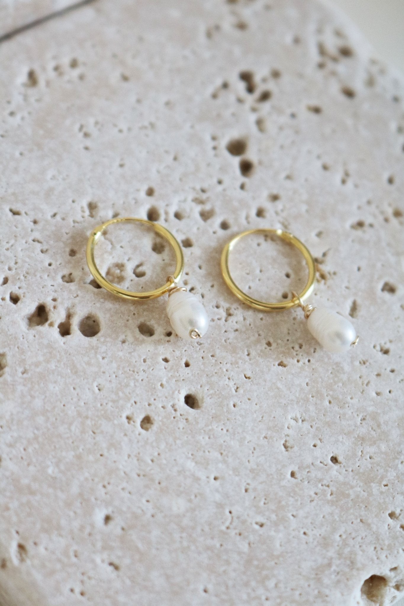 A Gold Filled Set of Dew Drop Fresh Water Pearl Hoops lay on Stone.