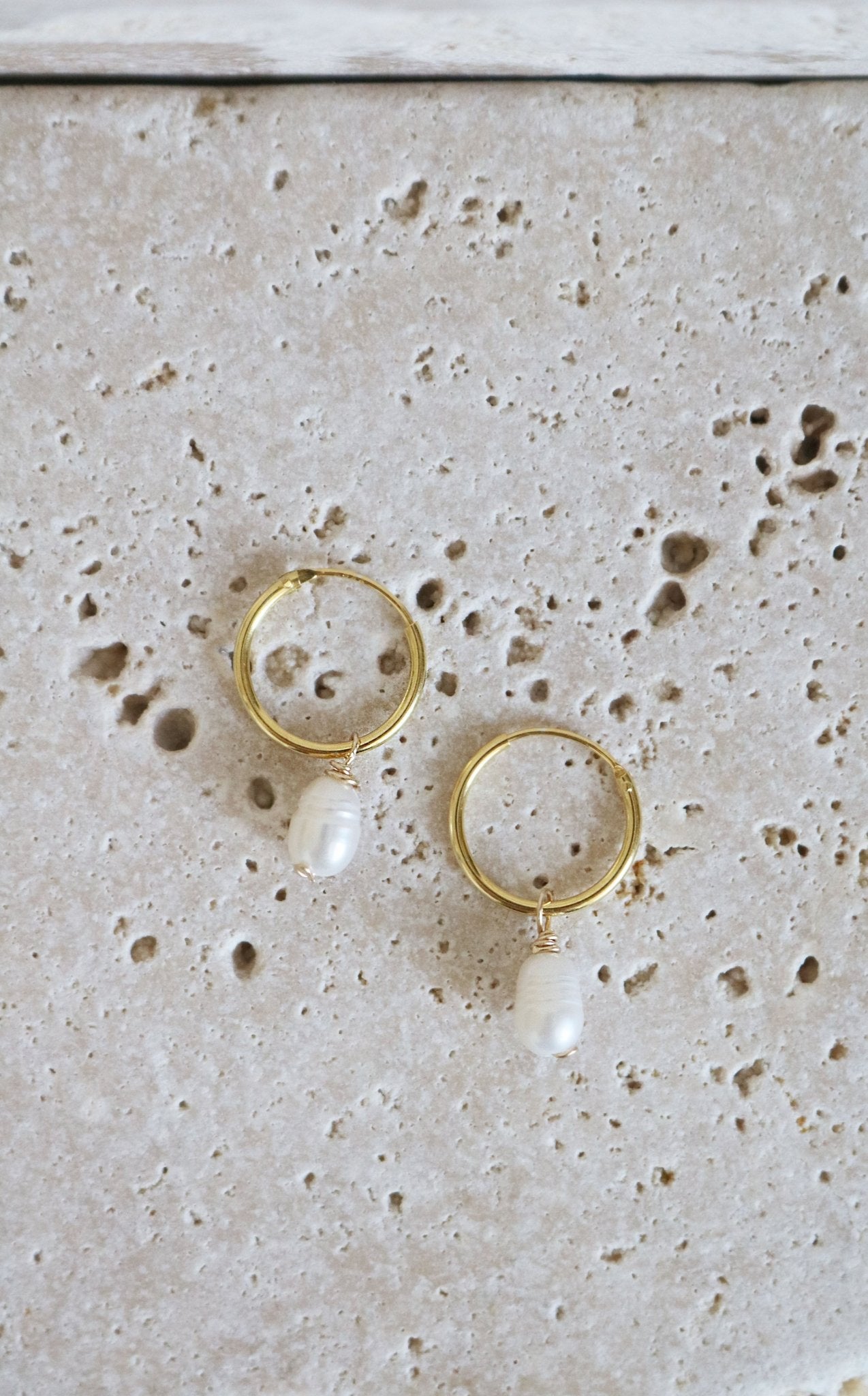 A pair of gold-filled bridal hoops with larger freshwater pearls displayed on stone.