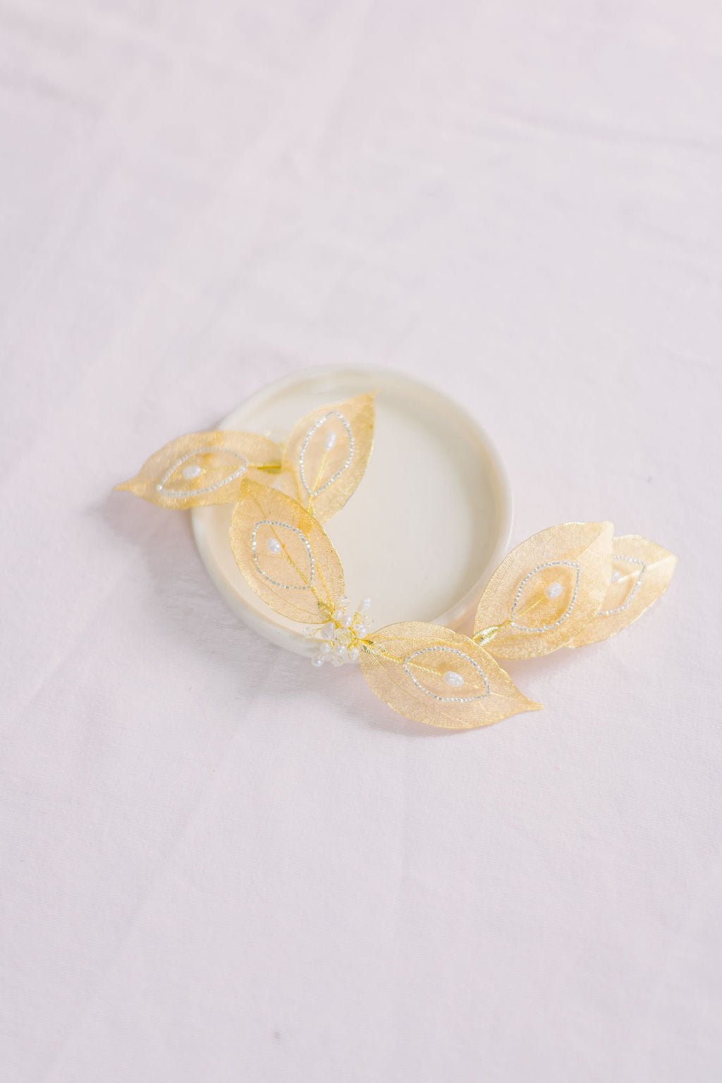 A gold leafy bridal hairpiece with freshwater pearls and crystals is displayed on a white background.