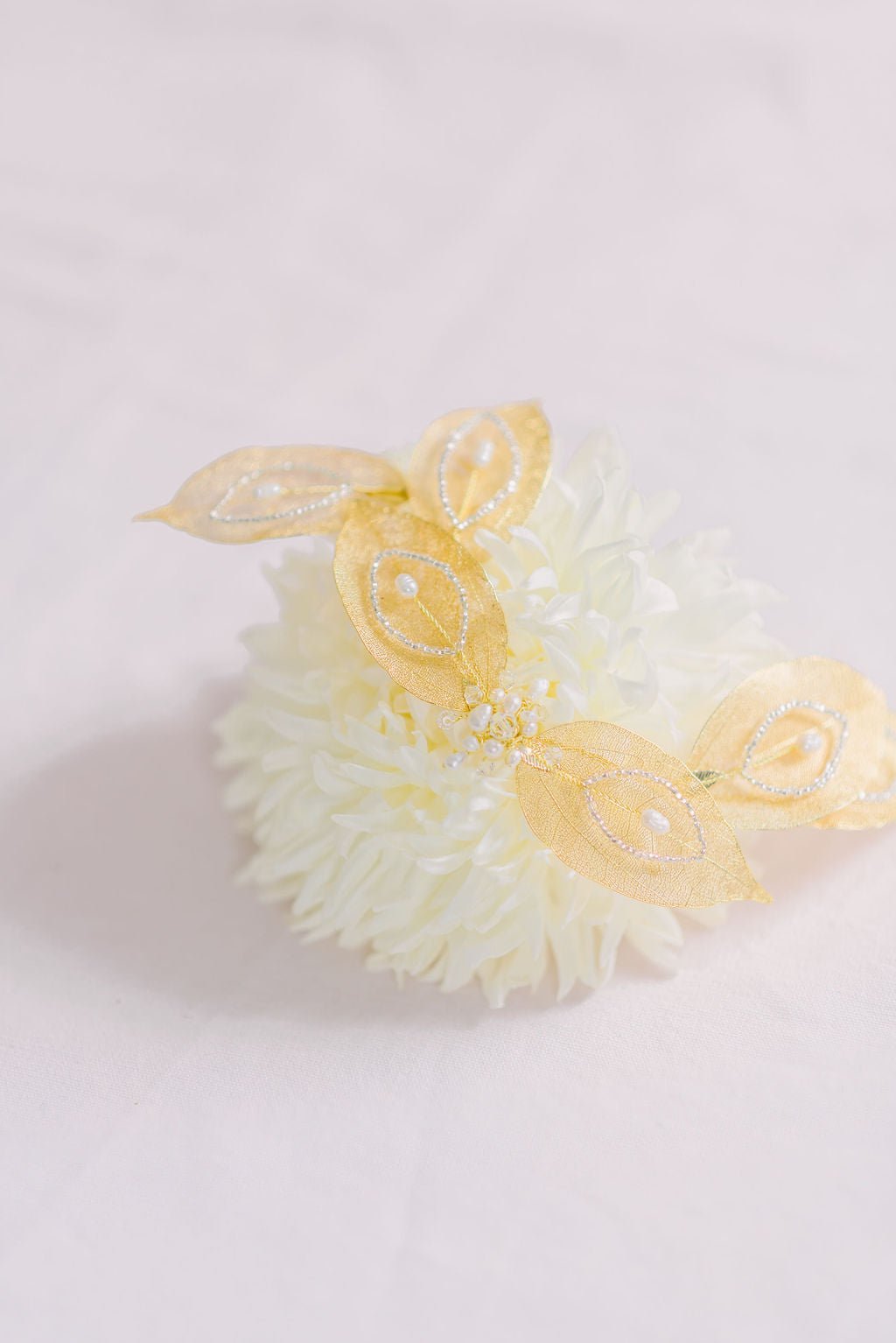 Golden leafed bridal hairpiece with fresh water pearls and crystals on top of a white flower. 