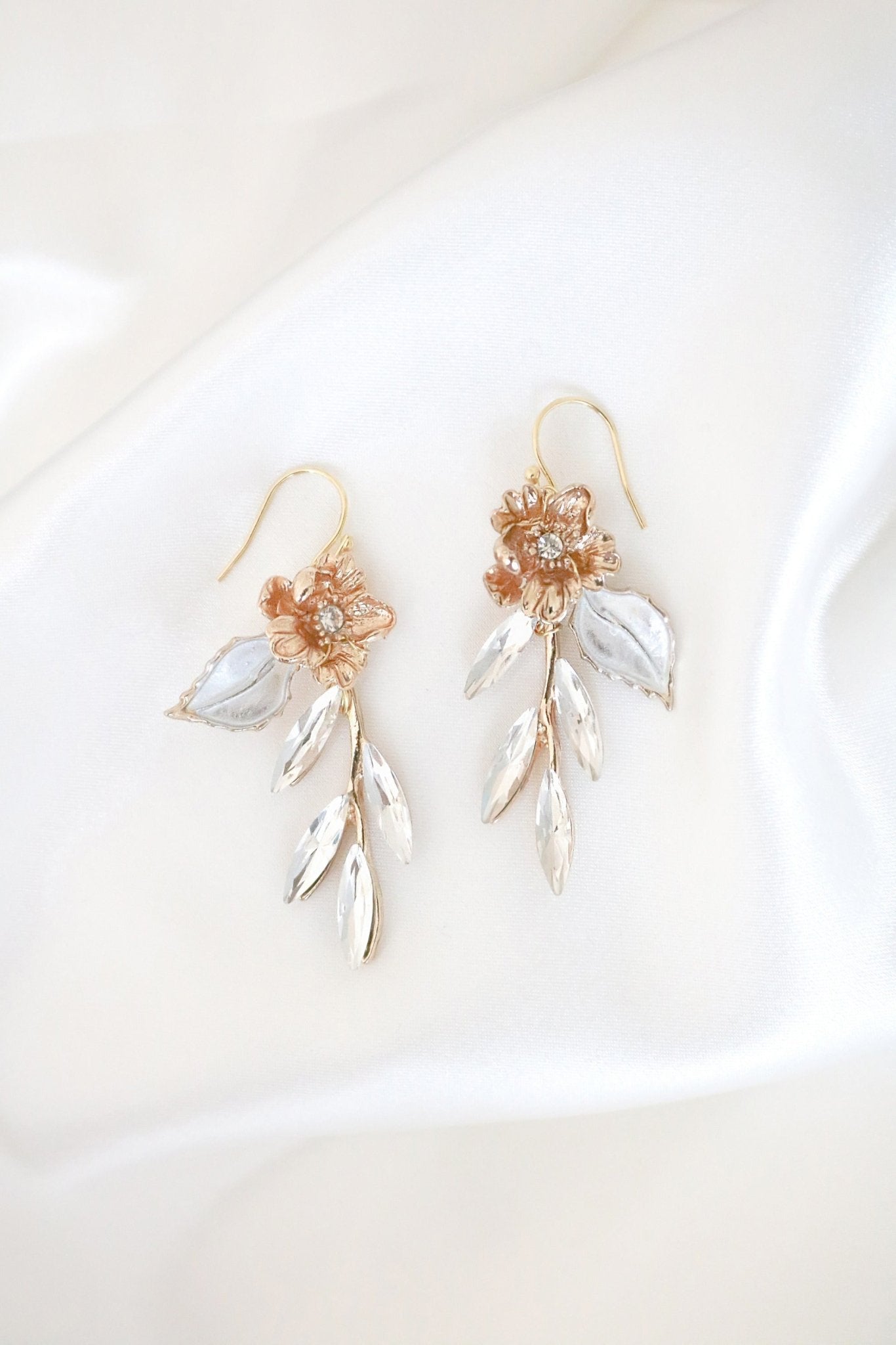 A pair of gold dangle earrings with crystal leaves on a satiny white background. 