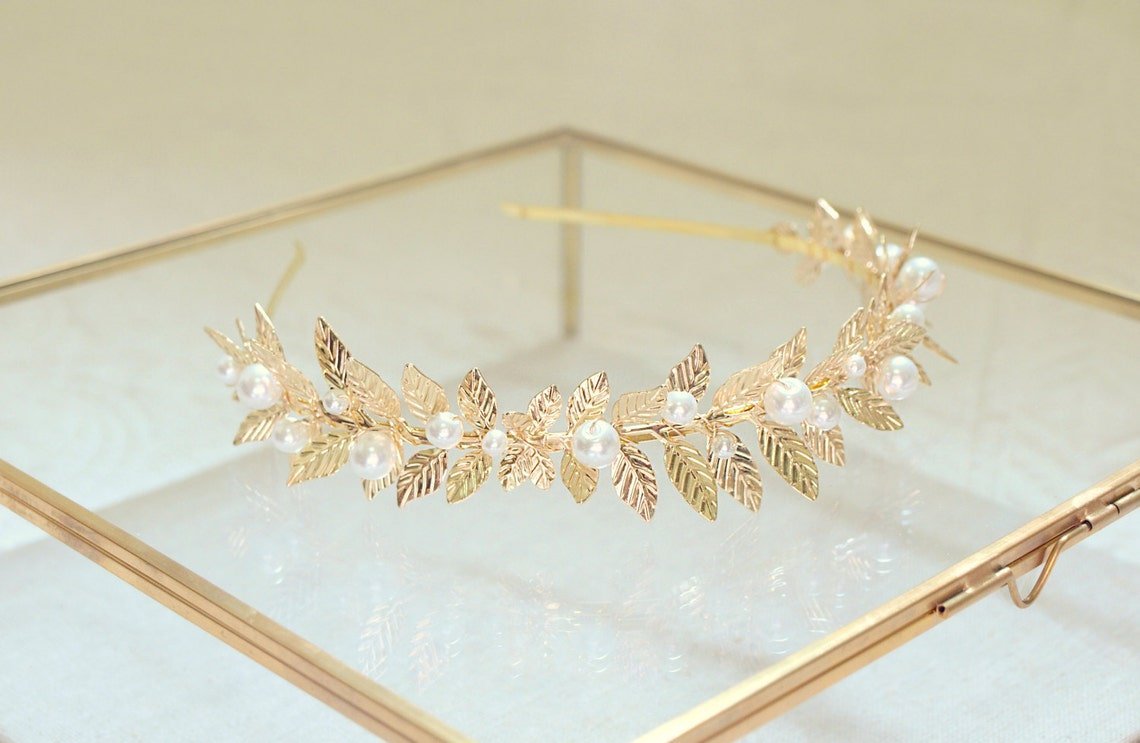 Golden headband with laurel leaves and freshwater pearls on glass display box. 