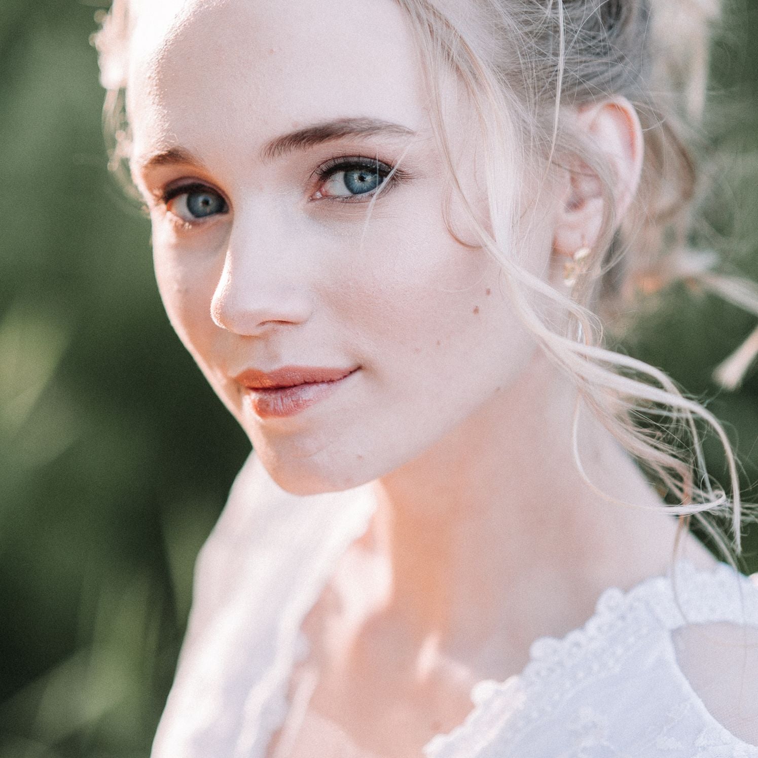 Close-up of a beautiful bride with blonde hair and vibrant blue eyes outdoors.