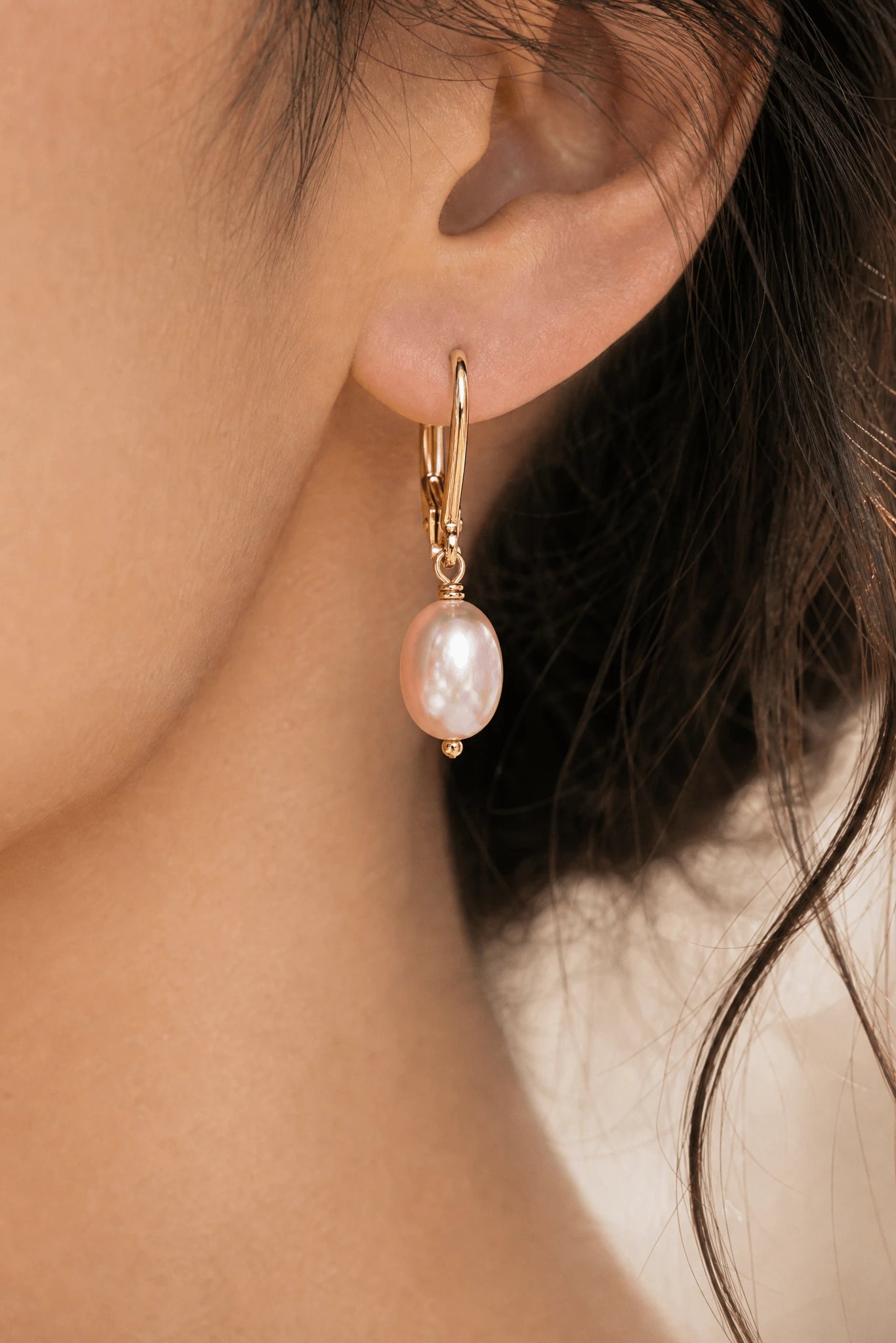 Extreme close up of a fresh water blush pearl  earring on gold filled leverback hook in woman's ear.