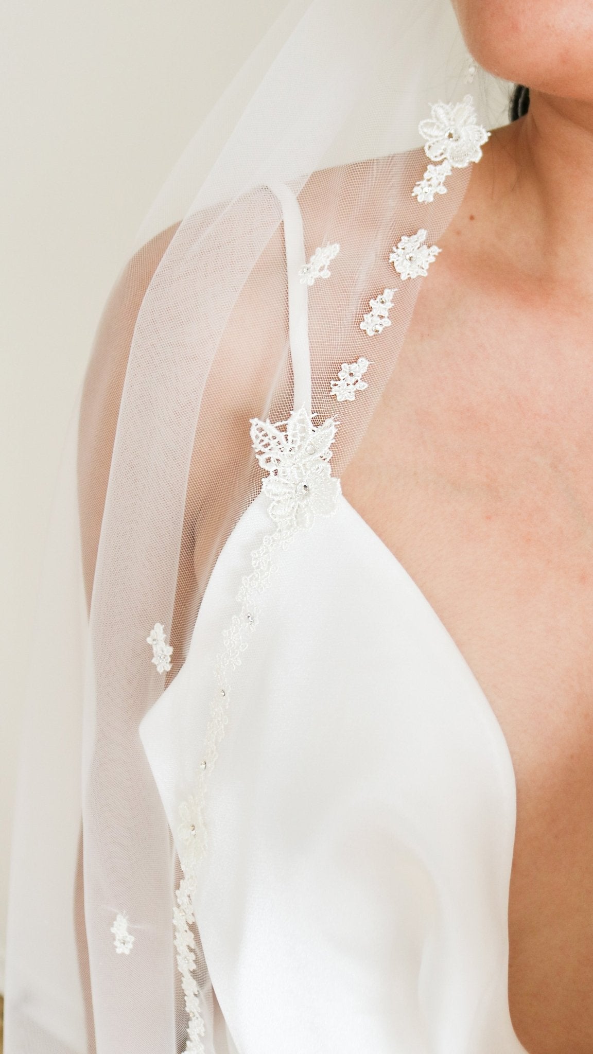 A bride's shoulder is covered by a tulle wedding veil with embroidered flowers. 