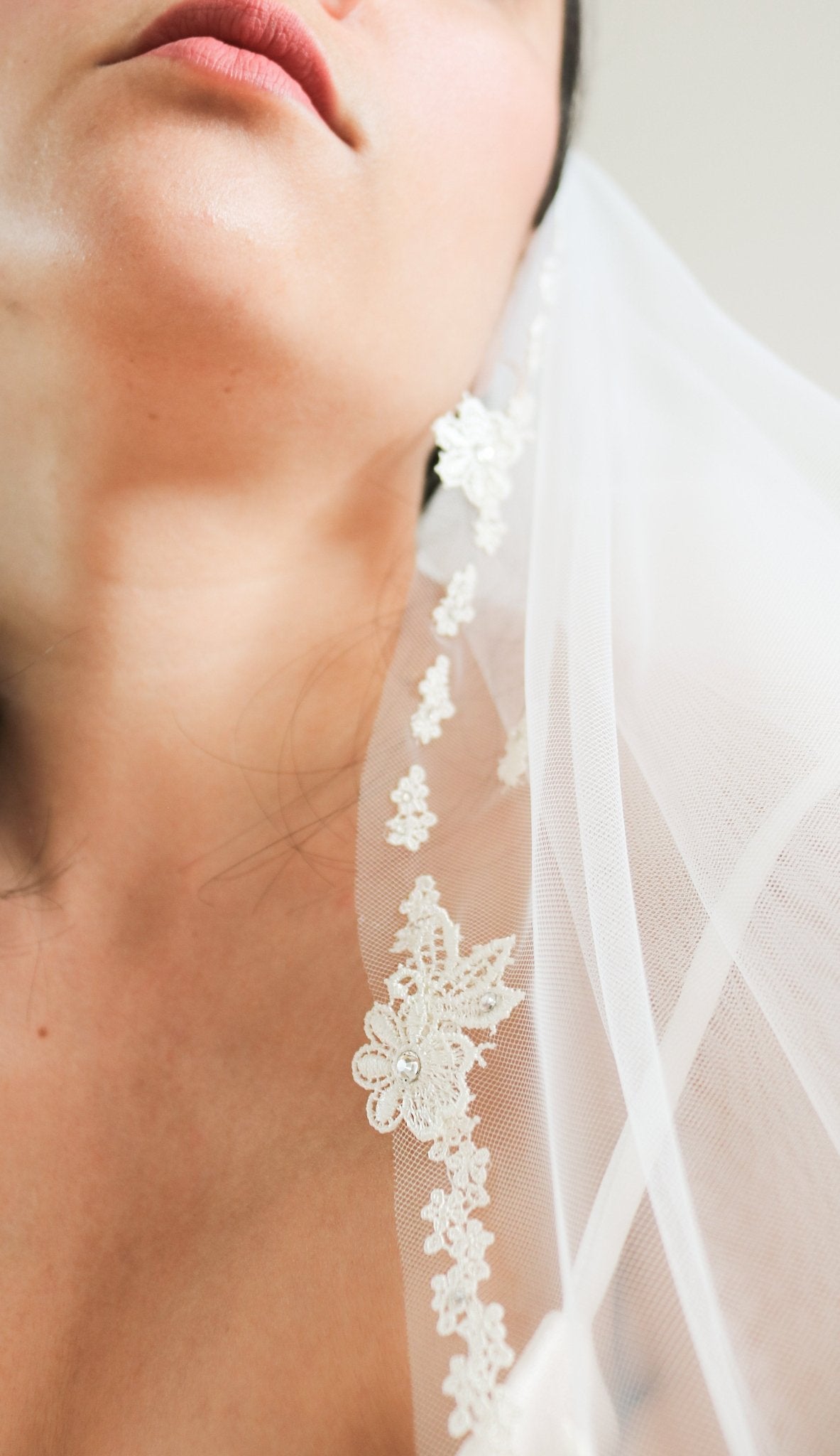 A close-up of the Eislyn wedding veil and its embroidered lace flowers that trails down the neck of a bride. 