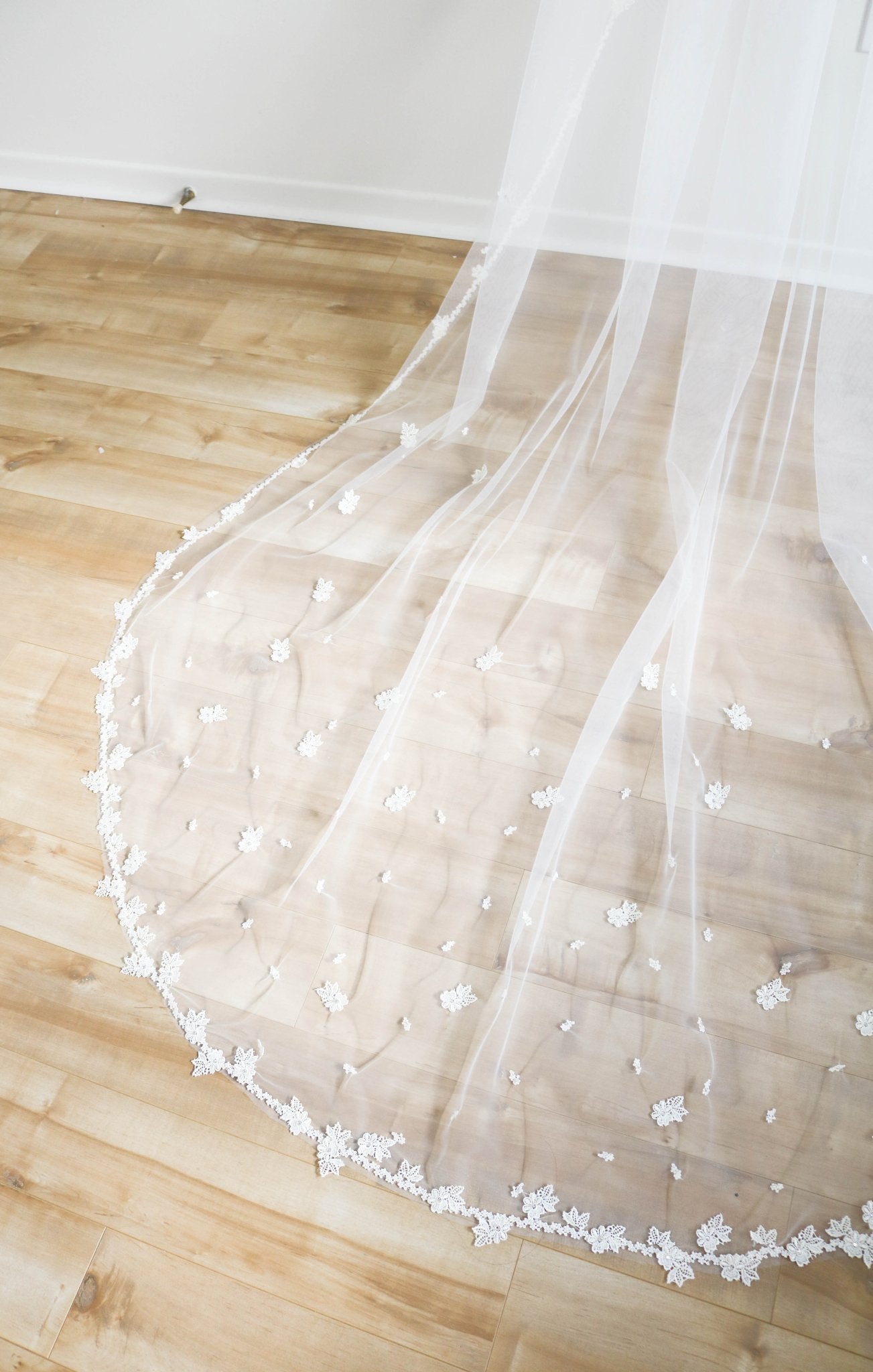 A close up of the detailed embroidered flowers on a wedding veil spread across a wooden floor. 