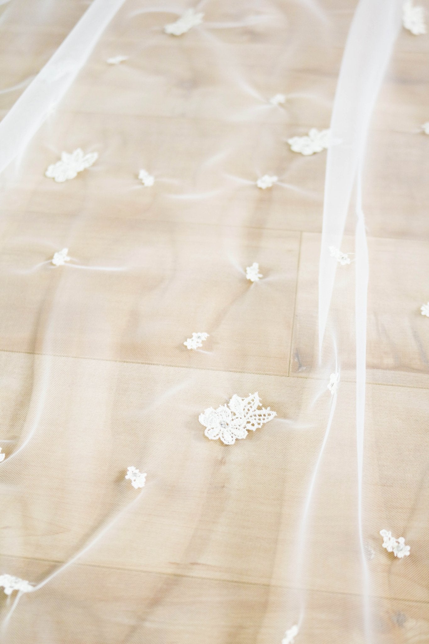 A close up of the detailed embroidered flowers on a wedding veil spread across a wooden floor. 