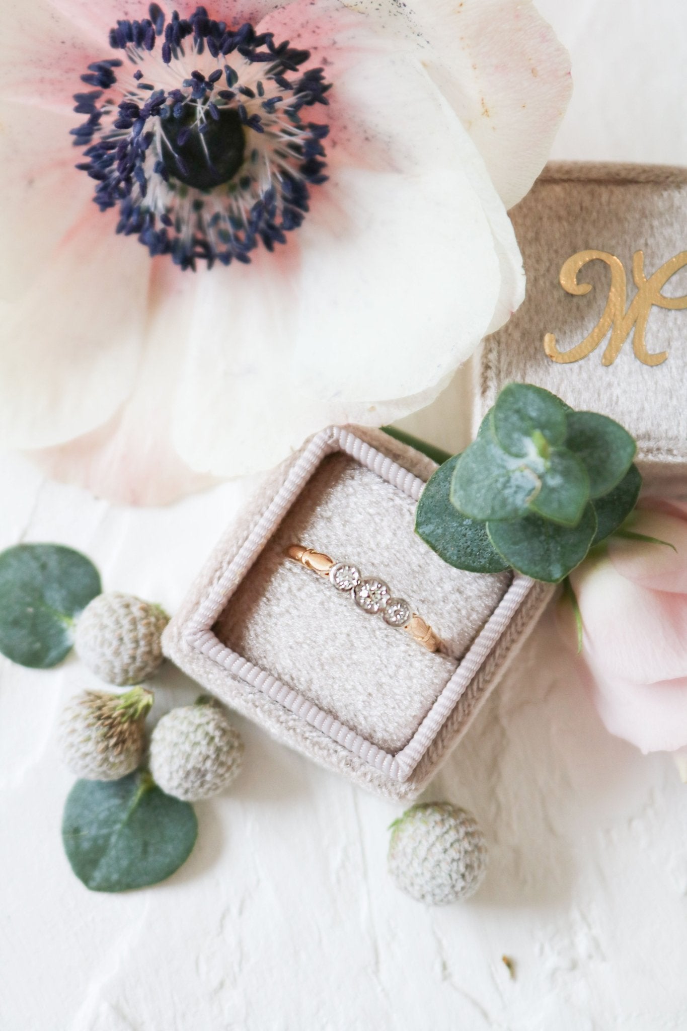 An Elara 18ct Yellow Gold and Platinum Diamond Trilogy Vintage Engagement Ring sits in a ring box with foliage. 