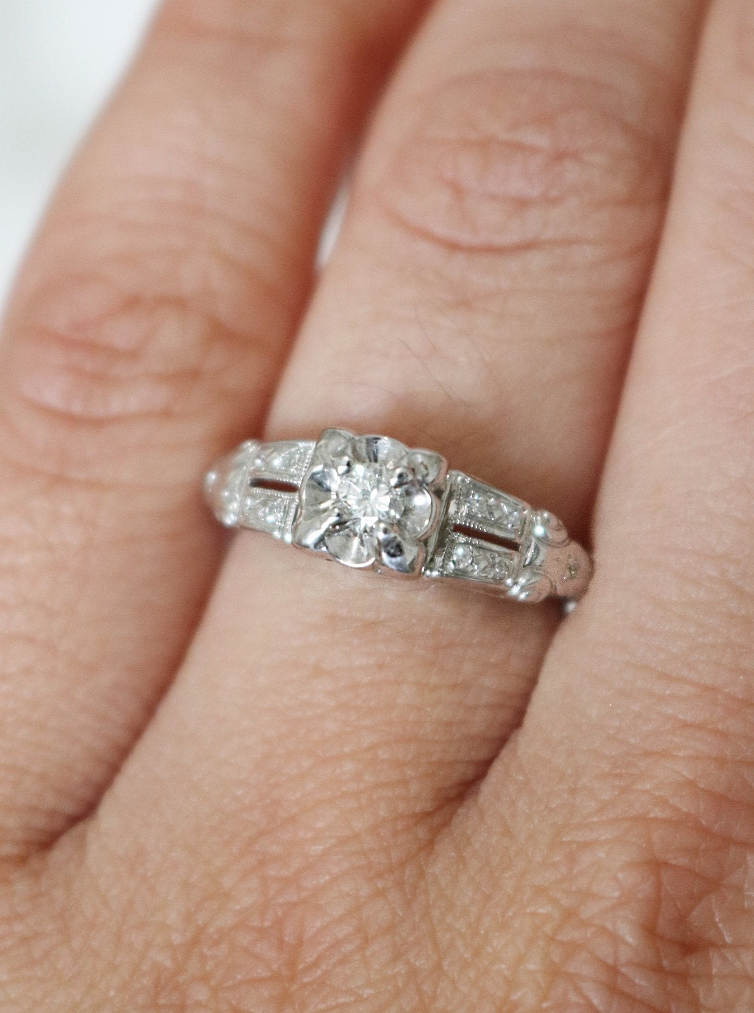 Extreme close up of a 14k White gold diamond vintage engagement ring on a ring finger. 