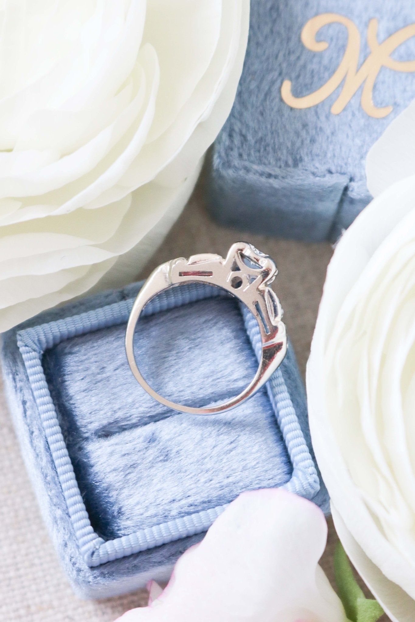 Side view of Elena Diamond Vintage Engagement Ring in 14k White Gold laying on top of a ring box surrounded by white roses. 