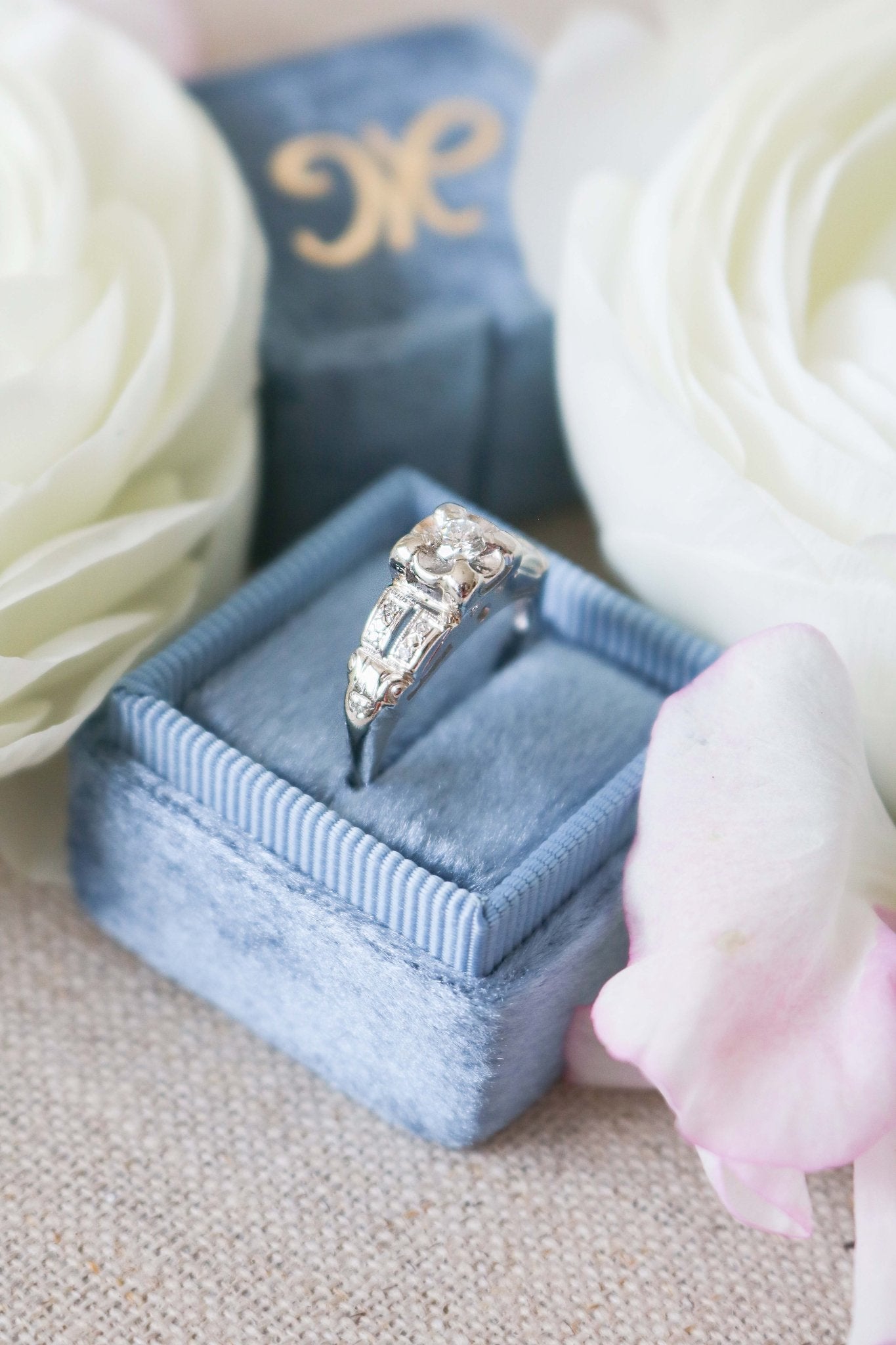 Close up of the Elena Diamond Vintage Engagement Ring in 14k White Gold sits in a ring box surrounded by flowers. 