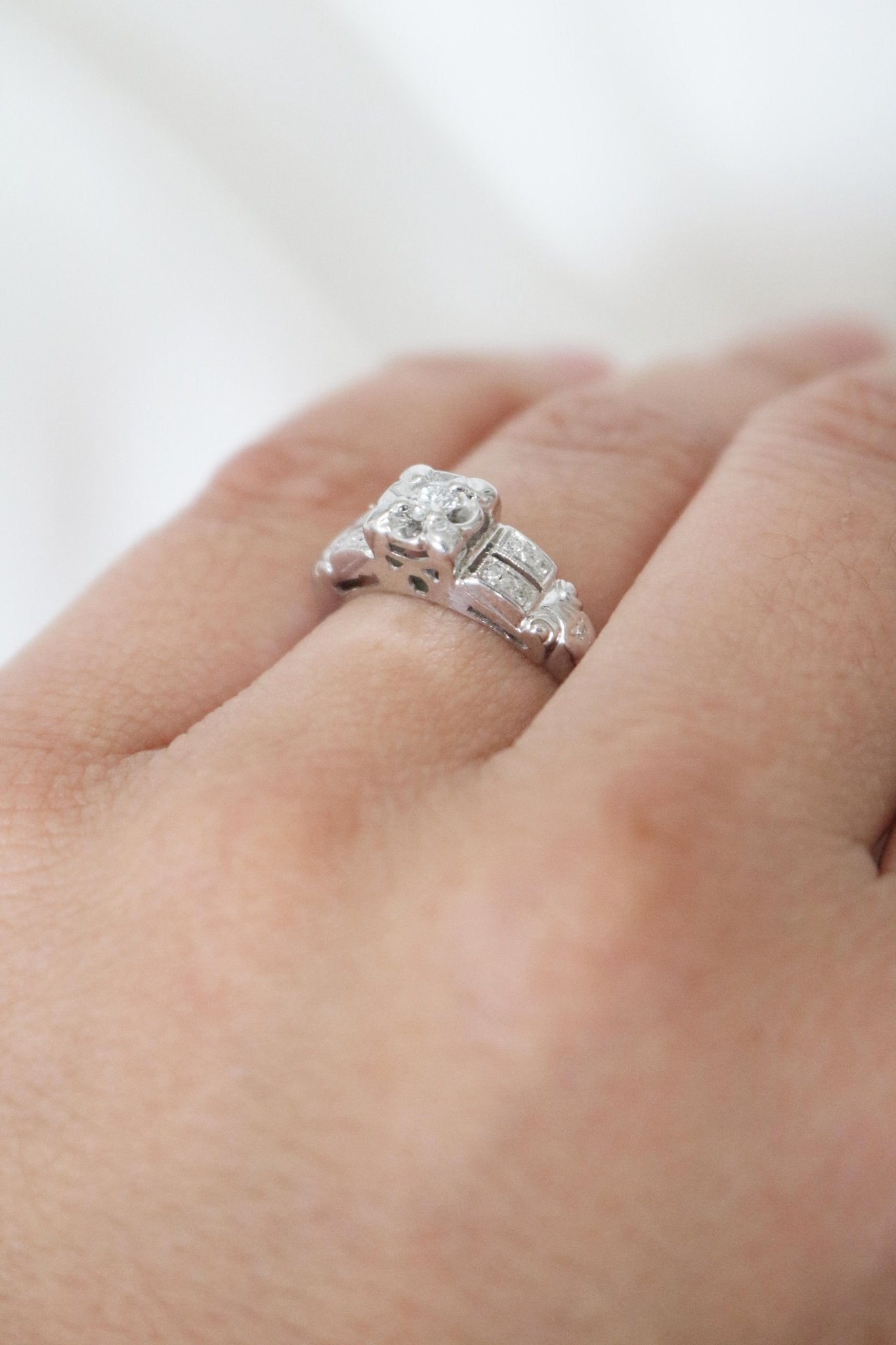 Extreme close up of a 14k White gold diamond vintage engagement ring on a ring finger. 