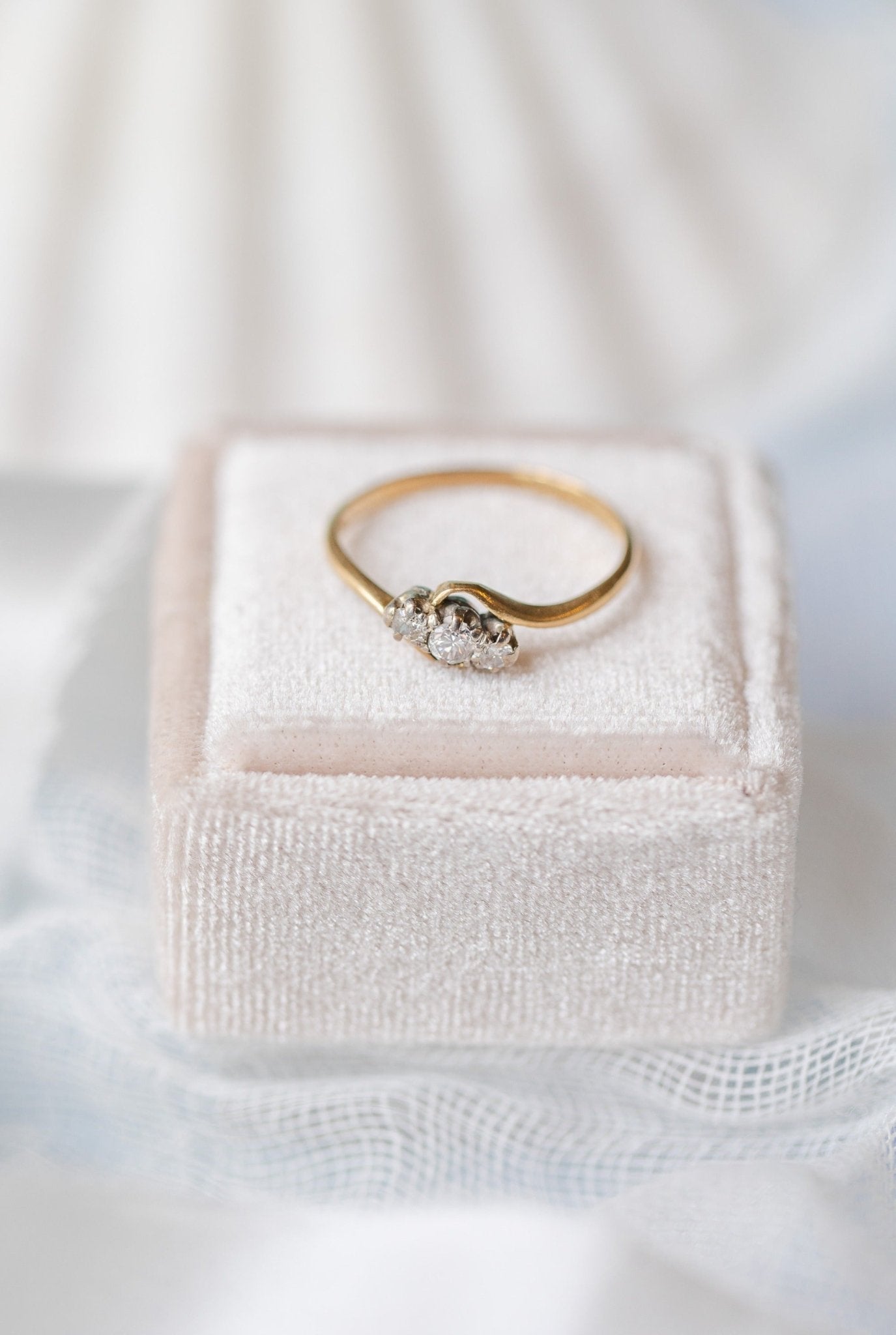 An Emilia Trilogy Diamond Engagement Ring in 18ct Gold and Platinum, c.1900 England sitting on a ring box against a white backdrop.