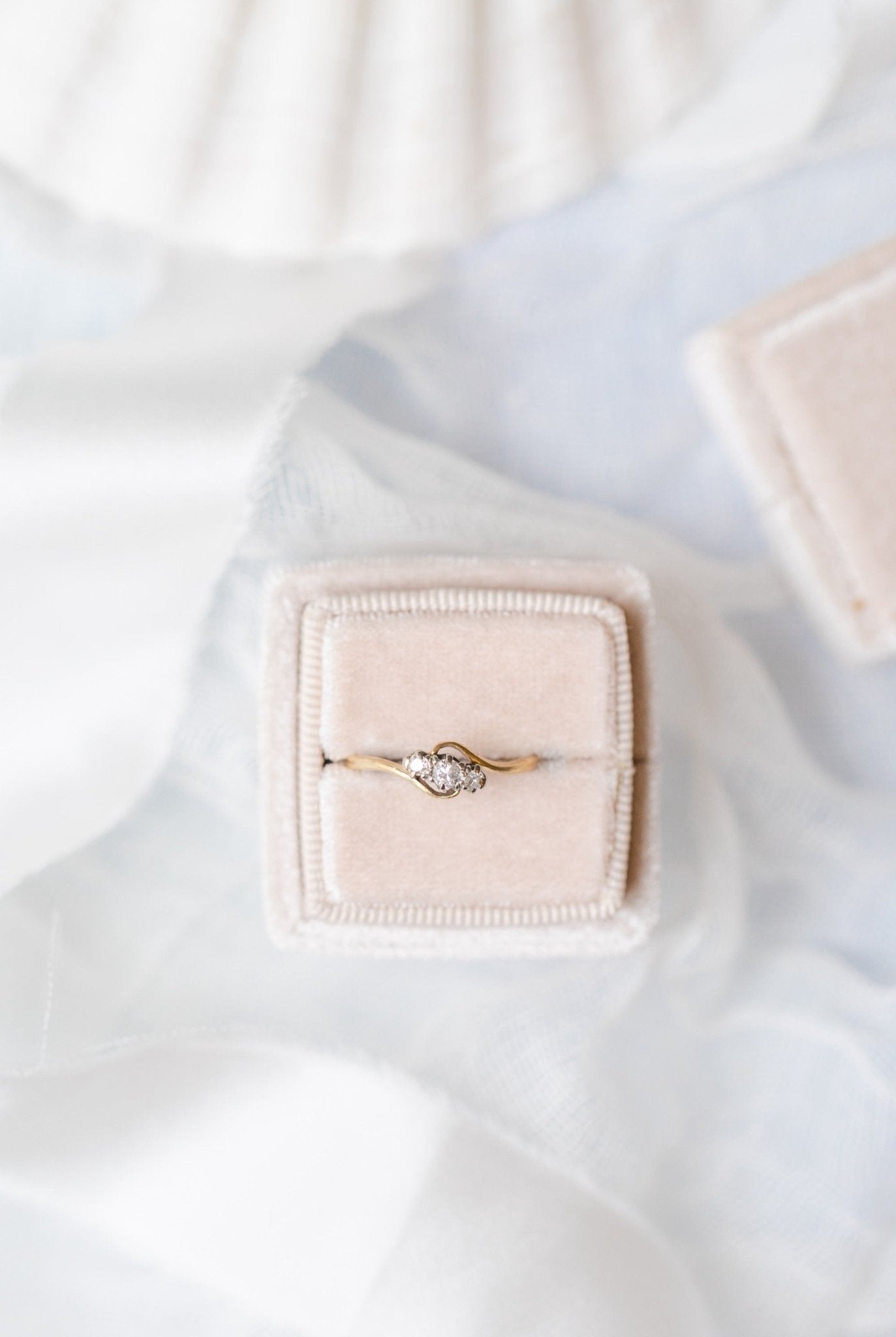 An Emilia Trilogy Diamond Engagement Ring in 18ct Gold and Platinum, c.1900 England sitting in a ring box against a white backdrop.