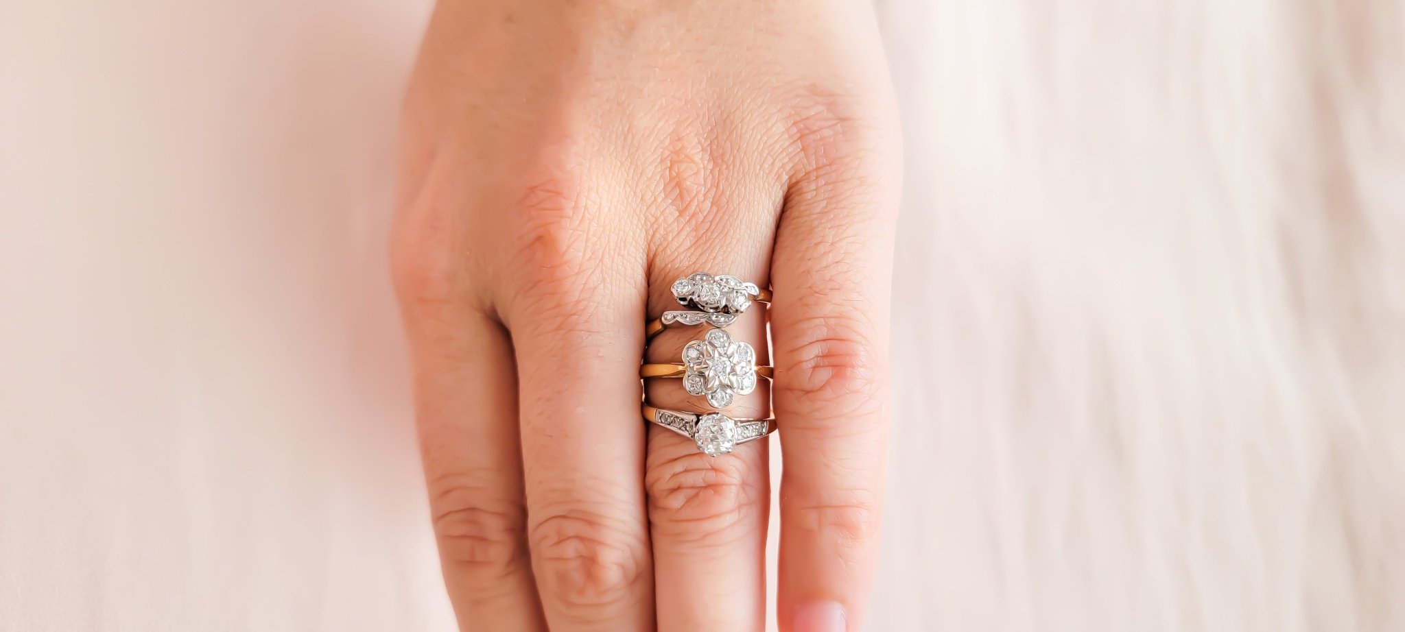 Three gold and diamond vintage engagement rings displayed on a ring finger. 