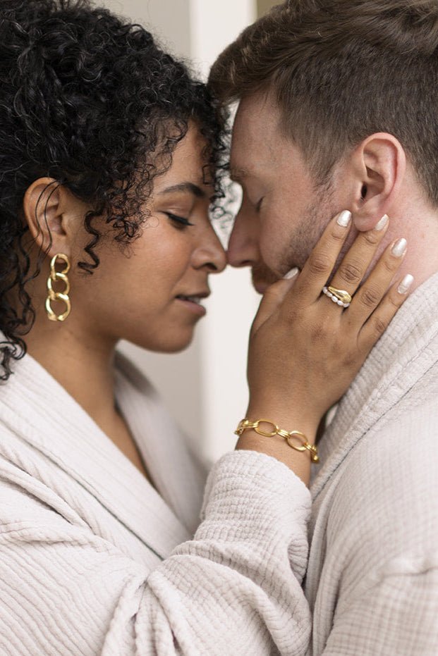 A woman holding a man's face while displaying her Essence Figure Gold filled Ring and The Everyday Freshwater Pearl Ring. Gold-filled jewelry Canada. Canadian jewelry designs. Pearl jewelry Canada.