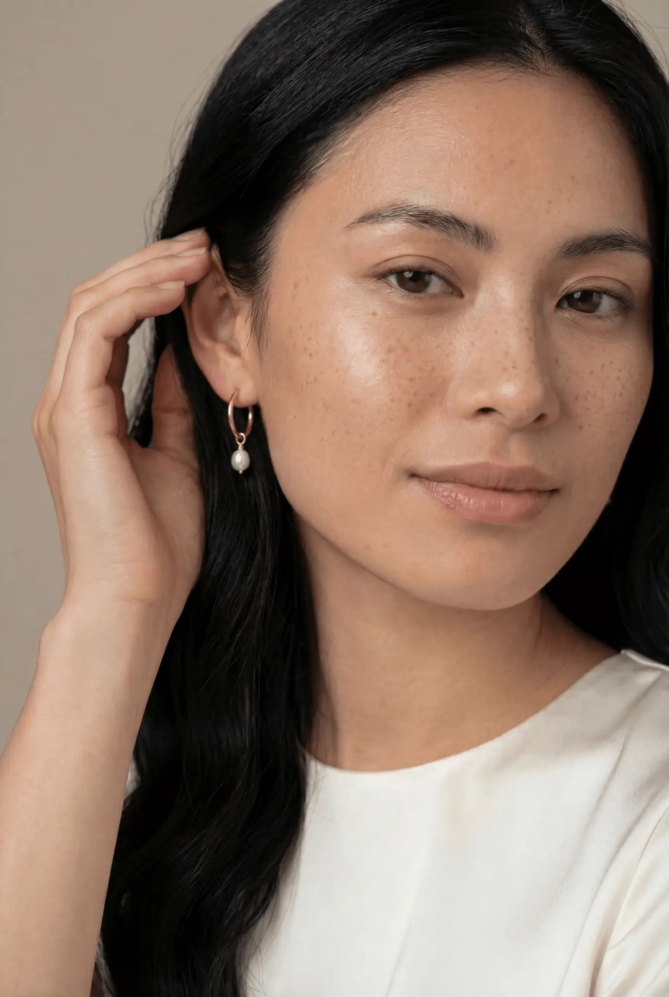 Filipina Woman wearing a gold-filled  freshwater pearl earring against a neutral background. Minimalist pearl jewelry handmade in Canada by affordable Canadian jewelry brand.