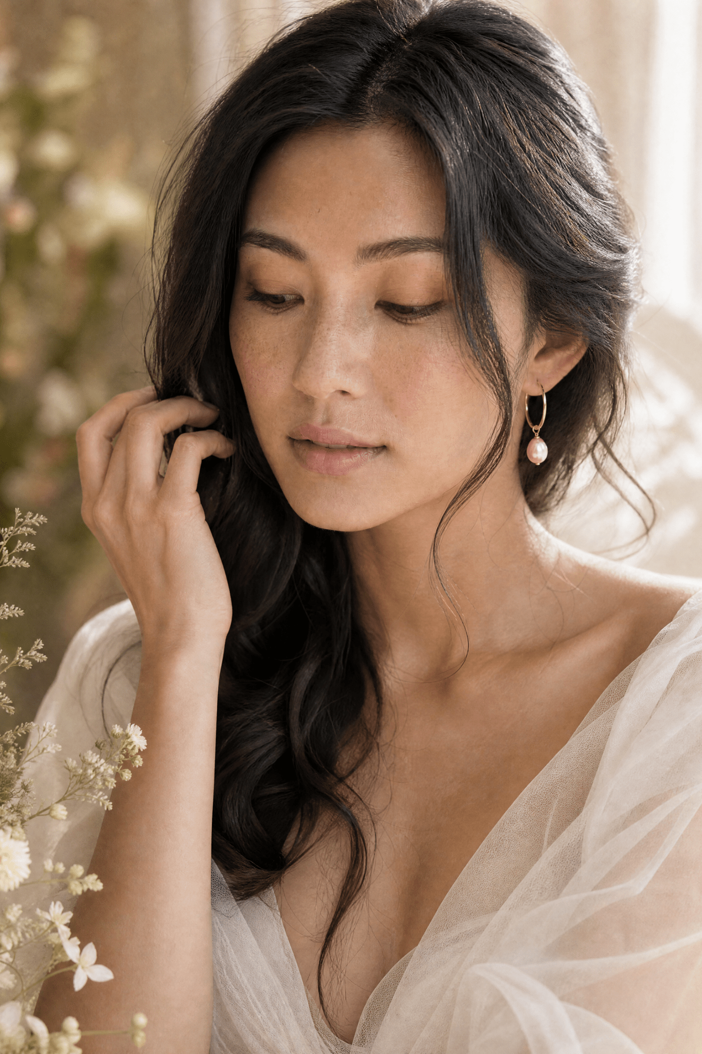 Filipino woman adjusting her hair with gold hooped blush pearl earring with a soft, blurred background. Handmade Canadian pearl jewellery