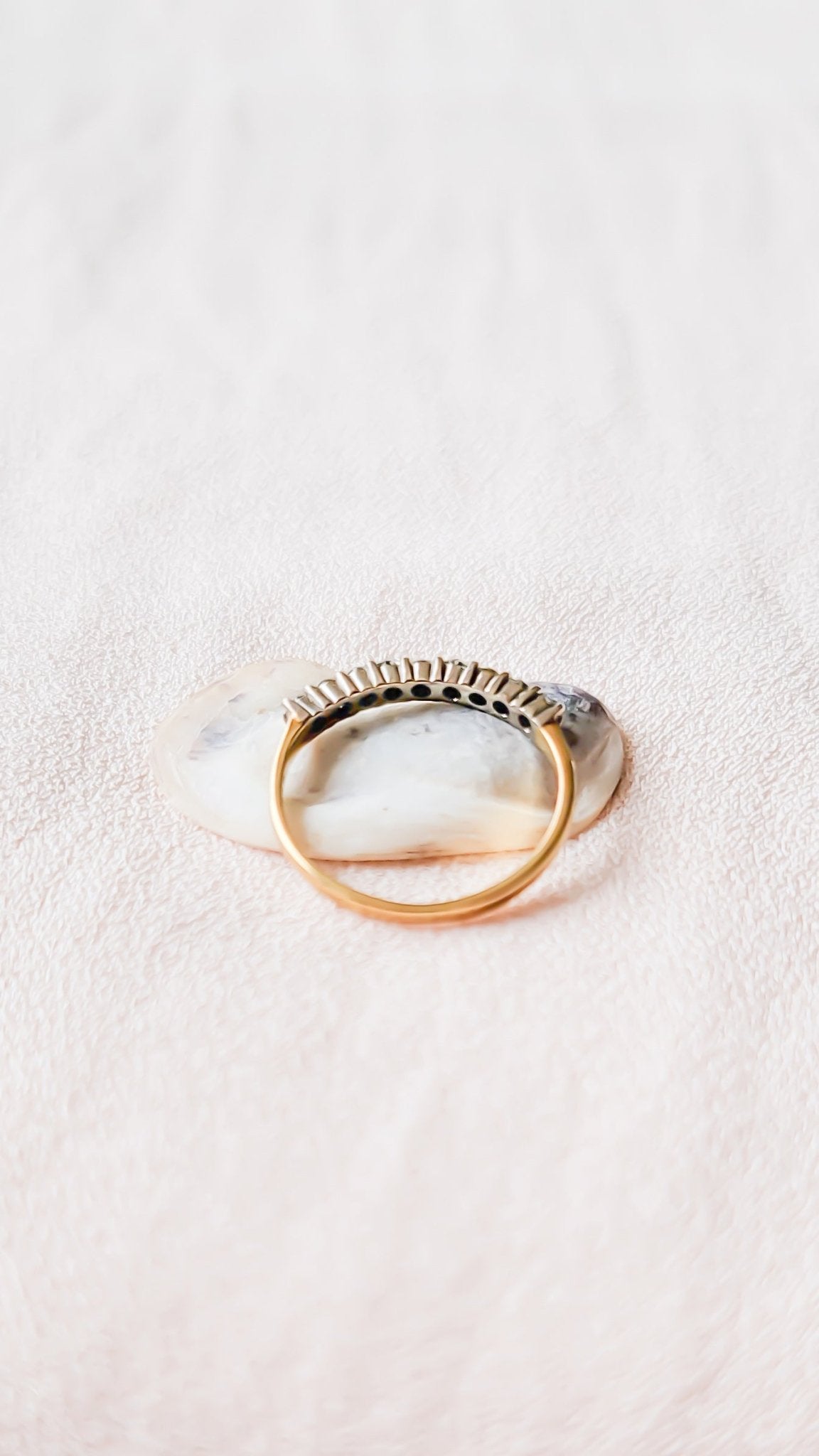 Side view of the Eva Half Eternity Vintage Diamond Engagement Band in 18k Gold c.1940s sitting on a seashell with a white background.