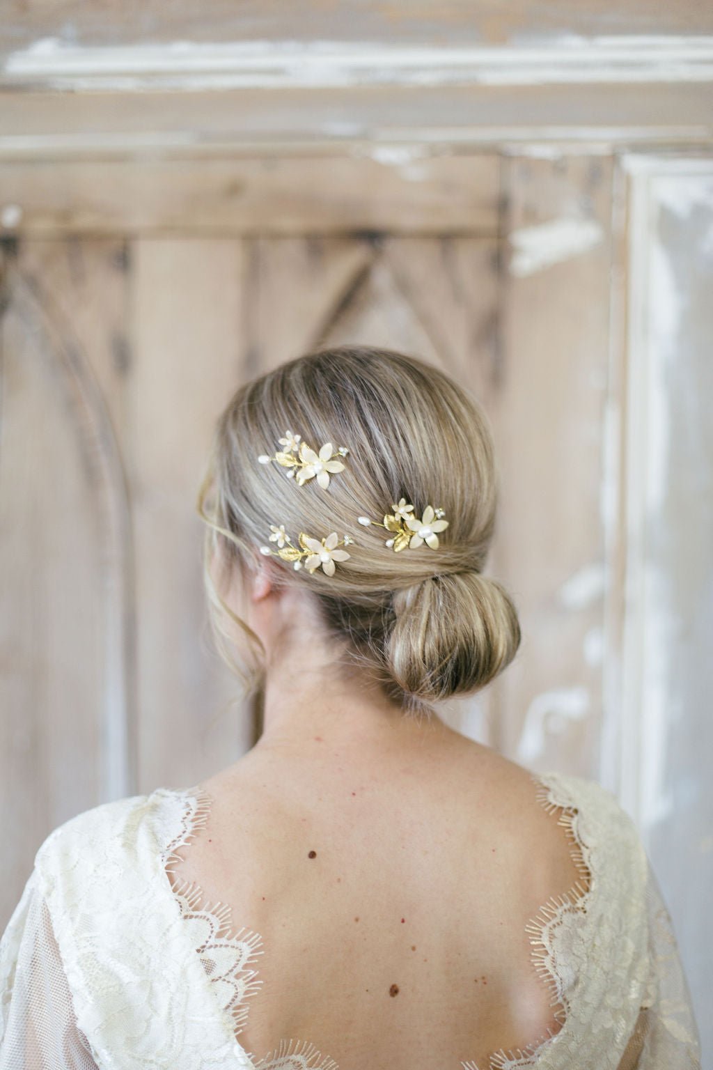 A bride by a rustic barn has an up-do holding three fancy floral hairpins with freshwater pearls. 