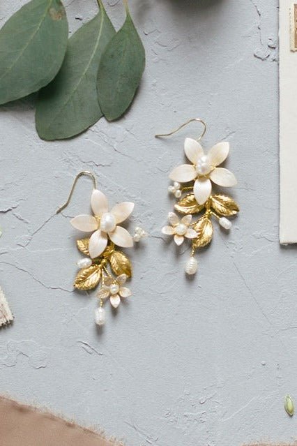 A pair of Evanthe Floral Bridal Earrings with Fresh Water Pearls and Enamel Flowers lay on a table. 