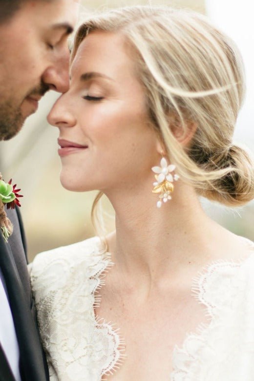 A blissful couple touch noses with the bride makes a statement by wearing floral gold-filled dangle earrings with organic freshwater pearls. 