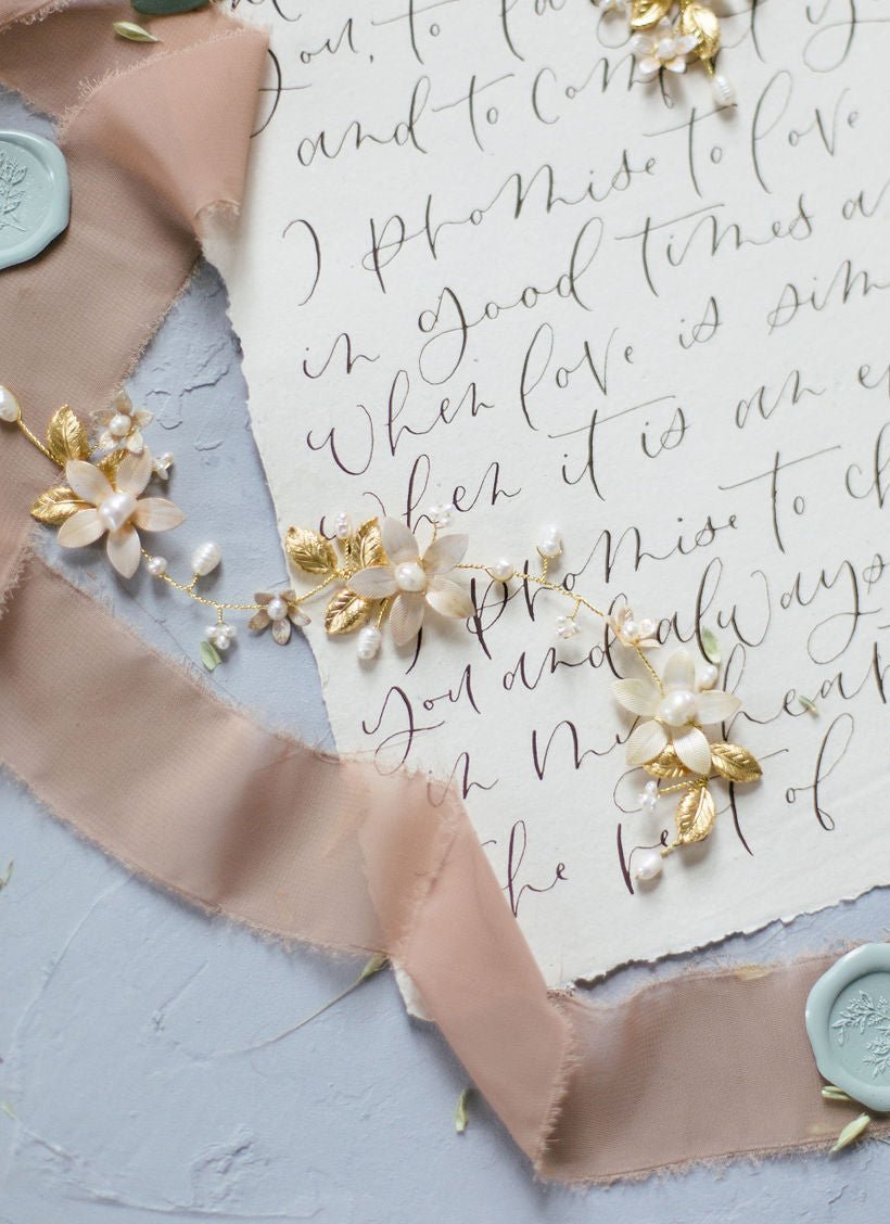 A gold bridal hairvine in gold with freshwater pearls and enamel flowers against wedding vows. 