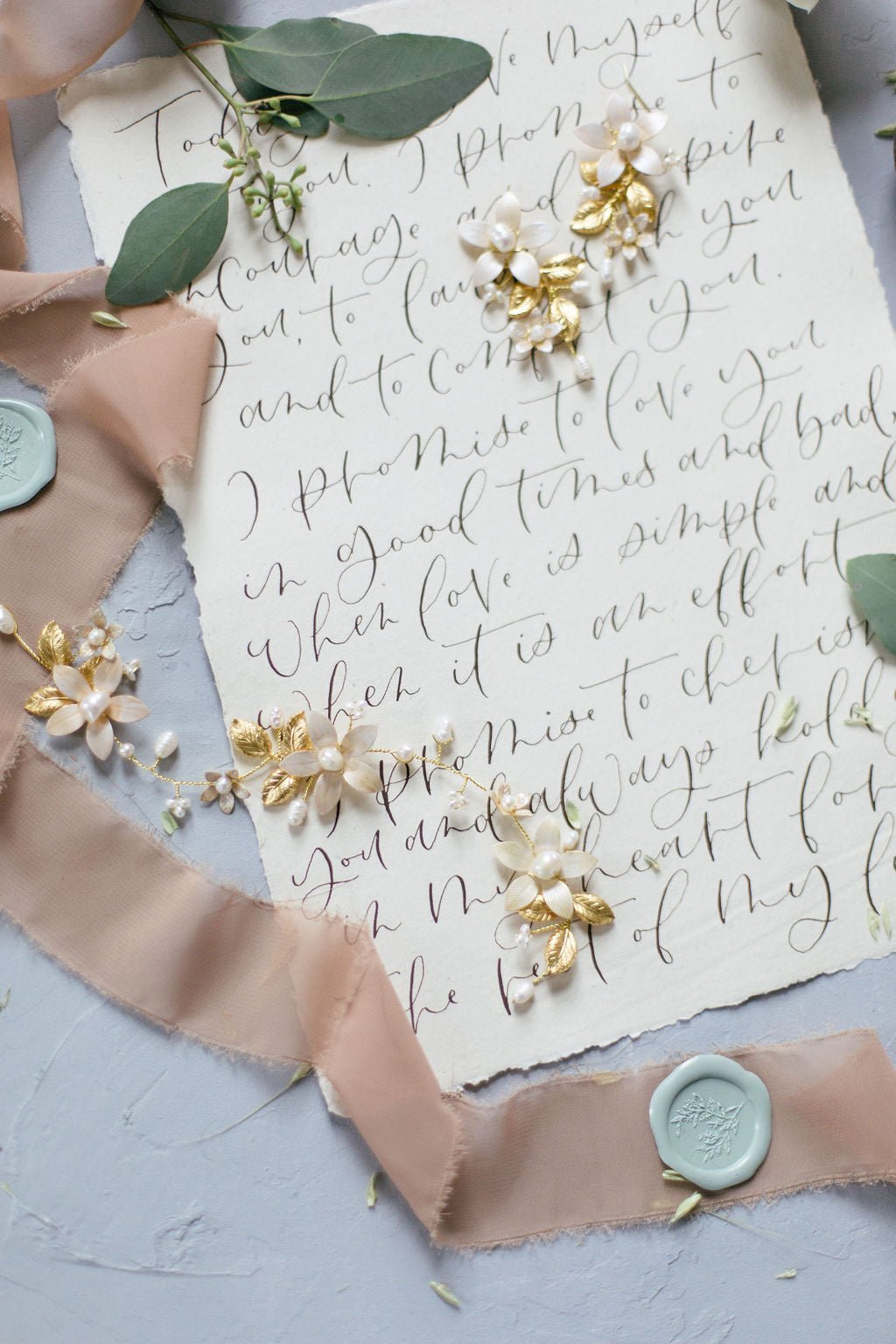 Evanthe Floral Bridal Hairvine with Fresh Water Pearls and Enamel Flowers paired with Evanthe Floral Bridal Earrings against a sheet of wedding vows. 