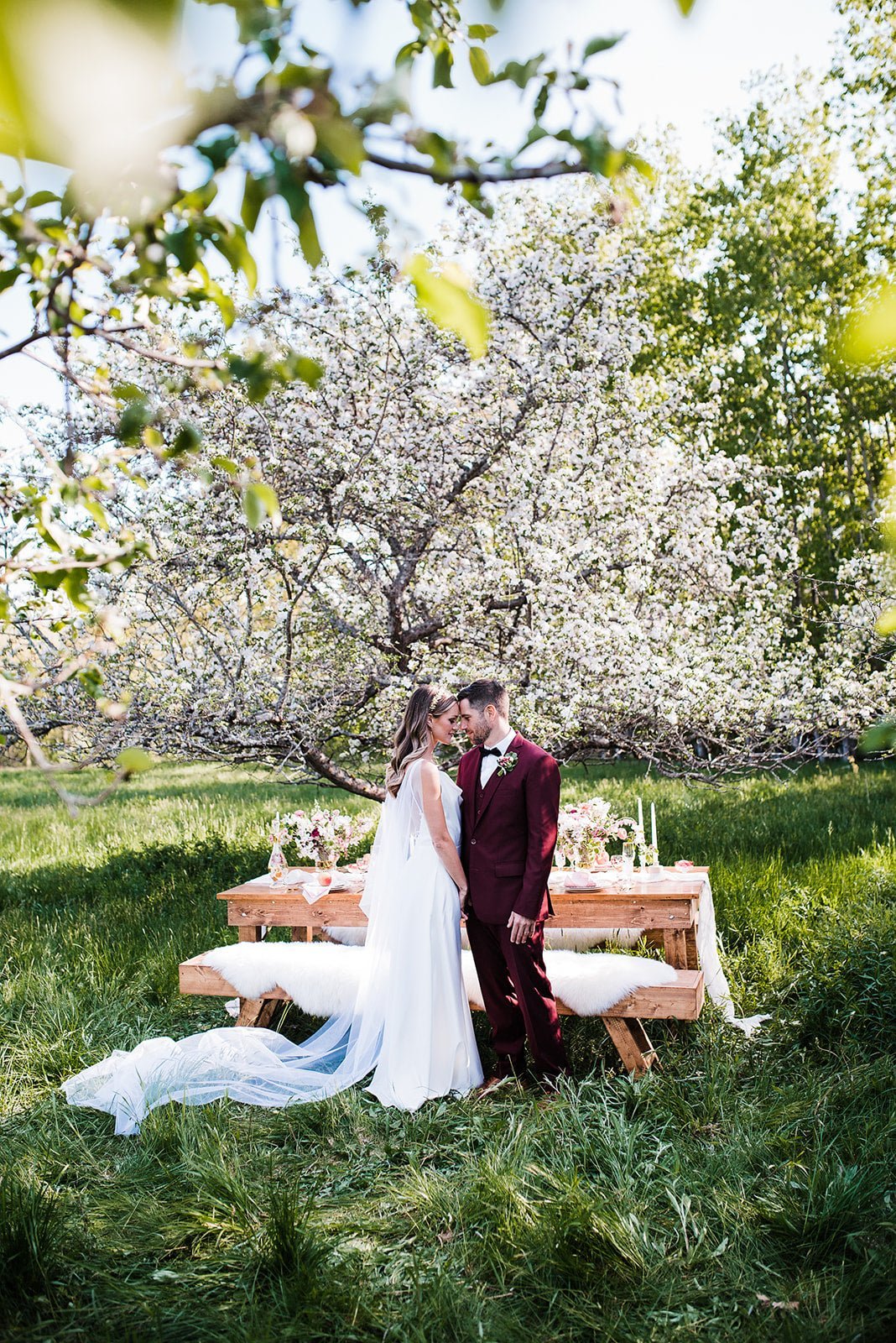 Bride and groom touch foreheads in a field. The bride's wedding veil trailing through the grass. 