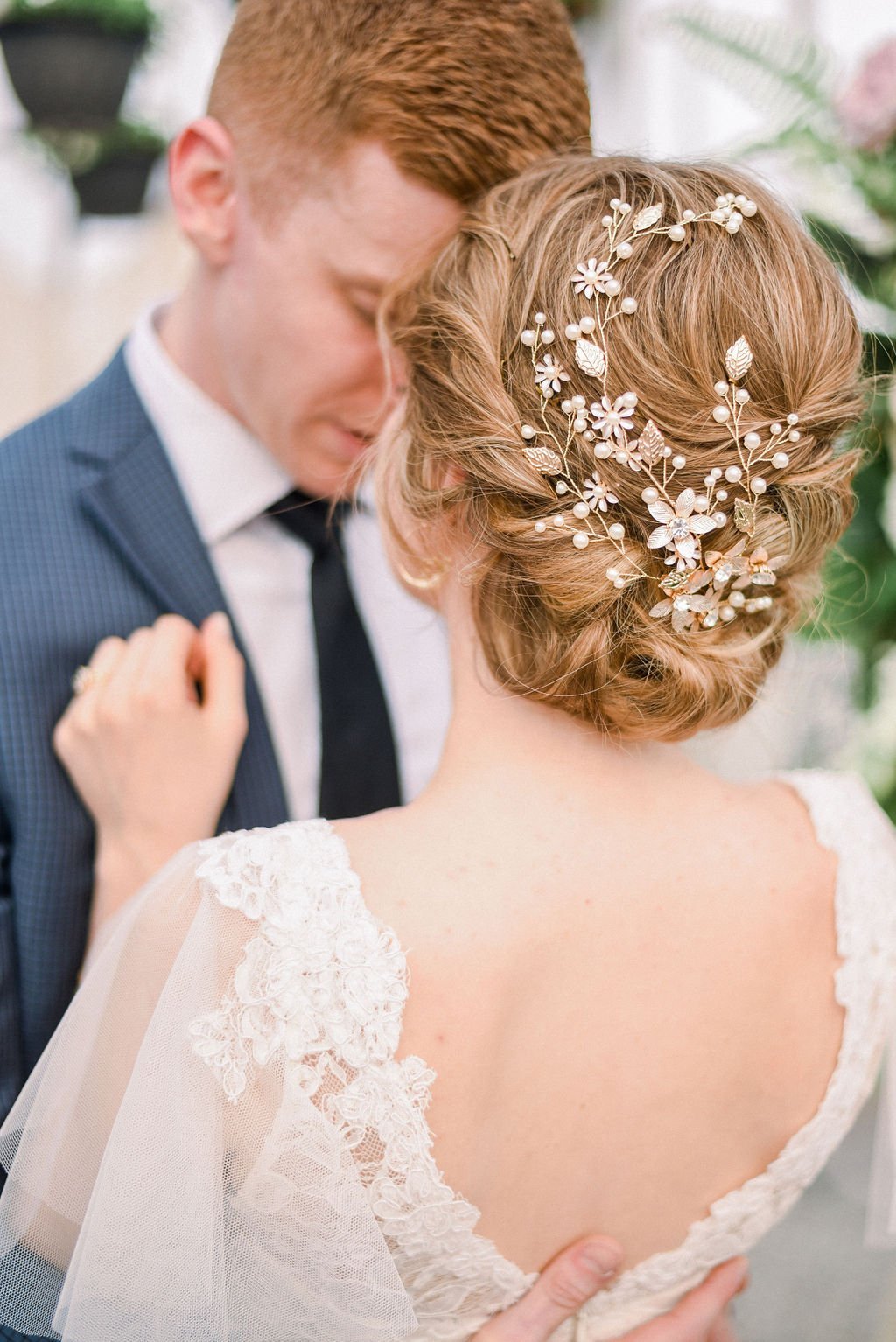 A bride and her groom embrace while she showcases her bridal hairpiece encircling her up-do. 