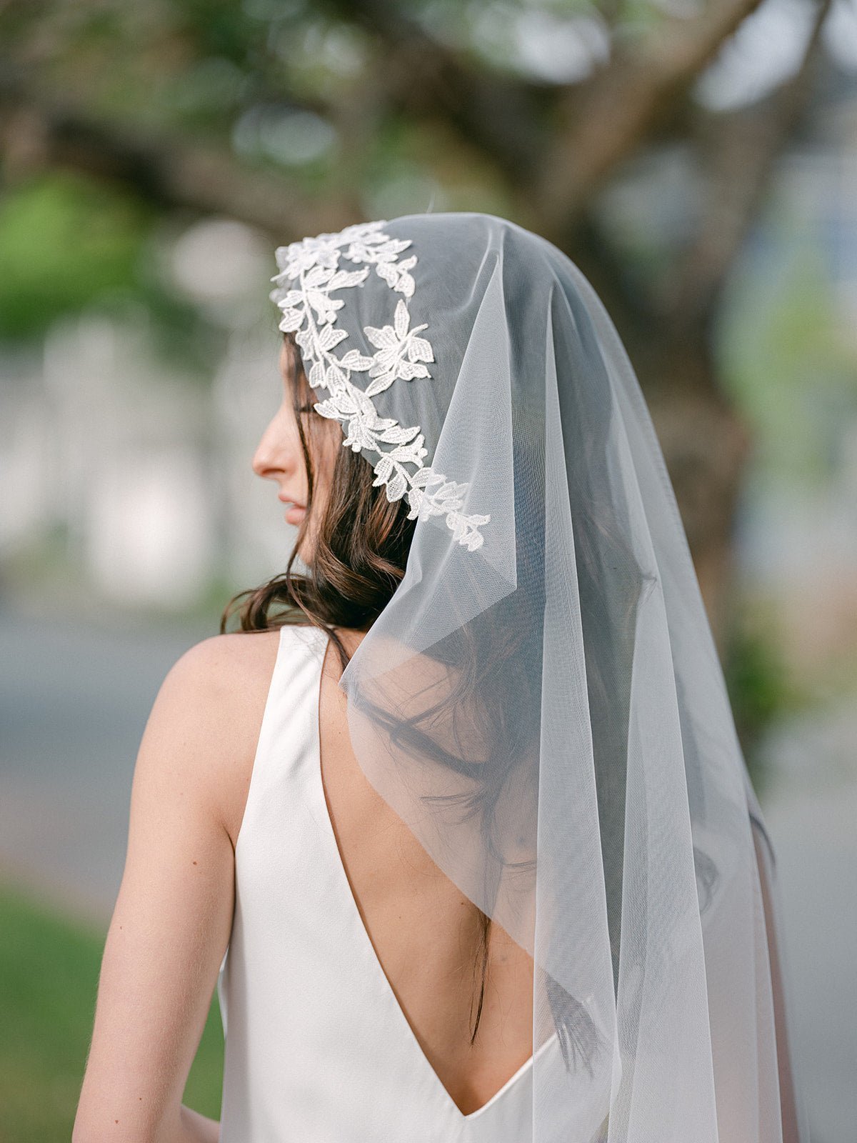 A bride looks down while wearing a lacey topped tulle wedding veil. 