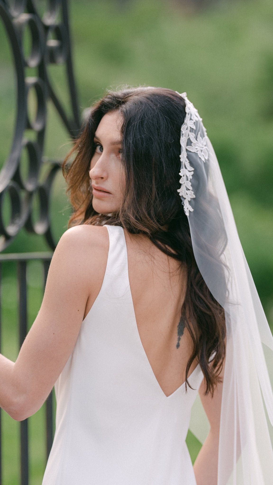 A bride looks over her shoulder; her Fable Mantilla Wedding Veil flows down her hair.